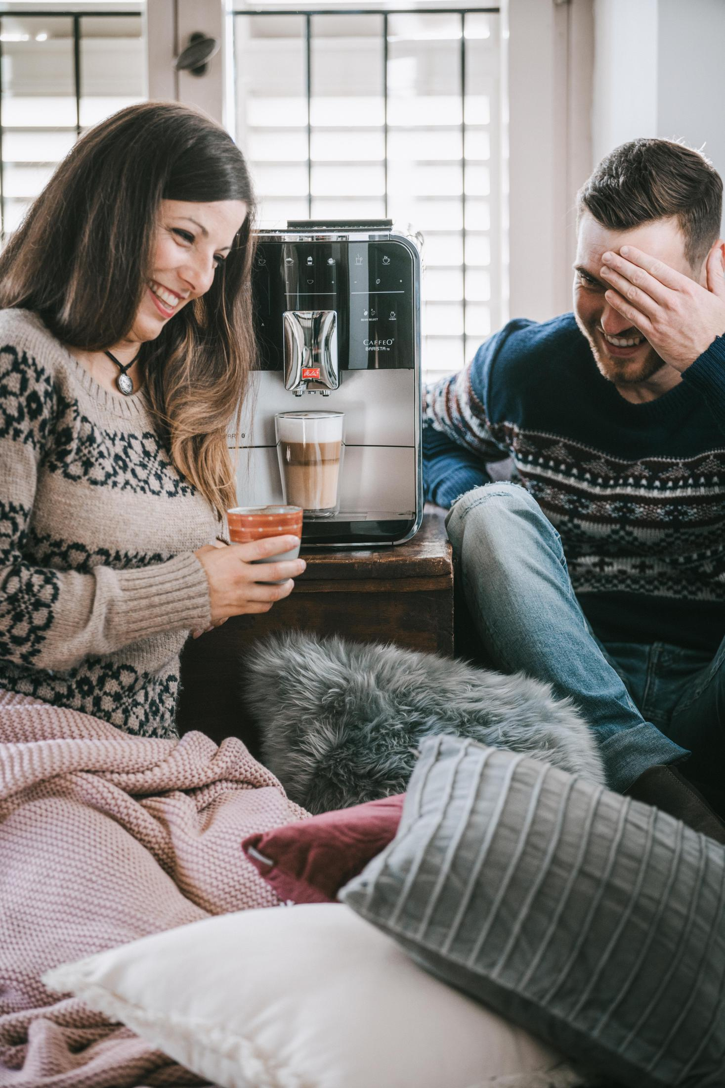 Paar lacht in der Nähe einer Espressomaschine. Ein Latte wird ausgegeben. Wohnraum.