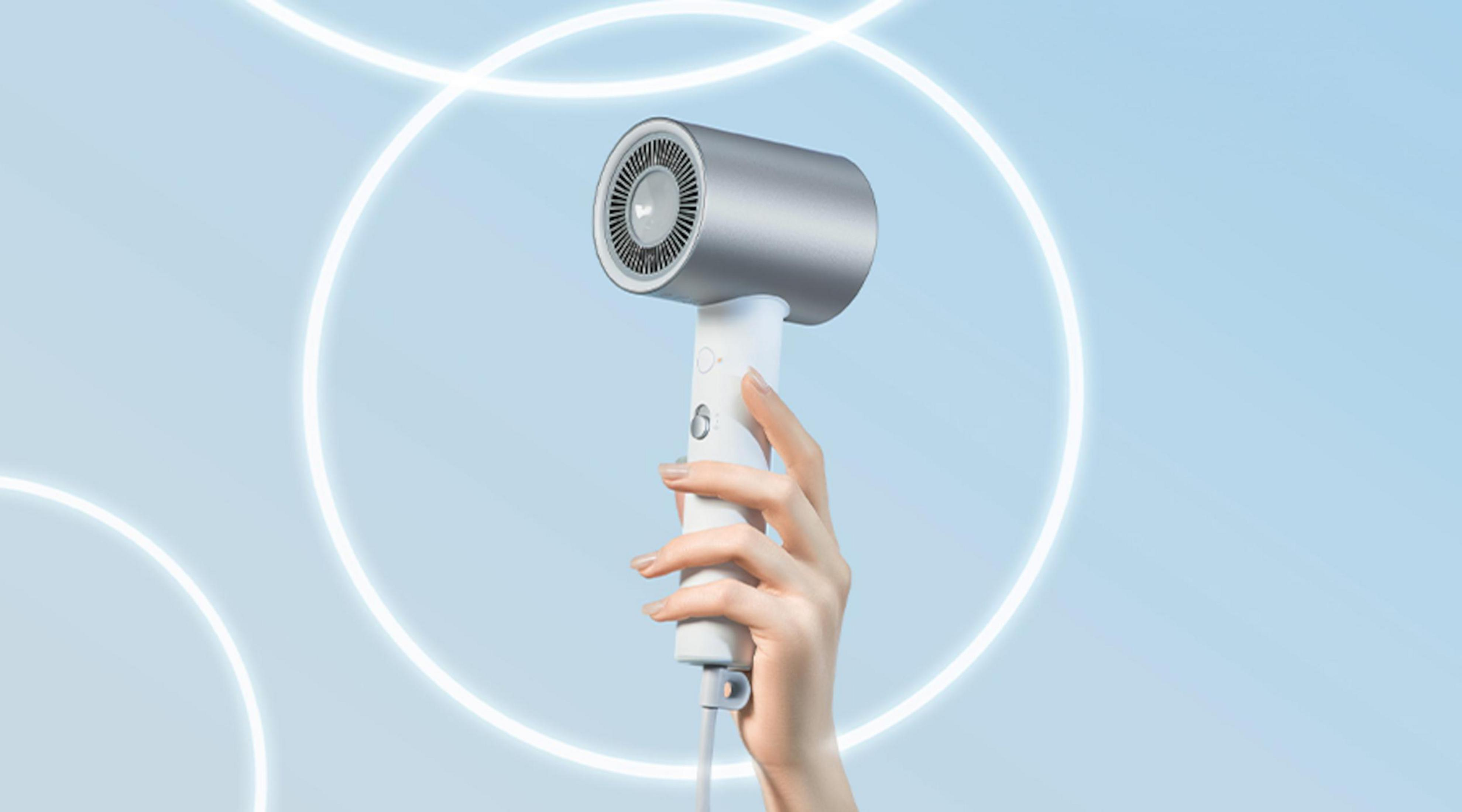 Ręka trzymająca srebrno-białą suszarkę do włosów, z niebieskim tłem i świecącymi białymi okręgami.