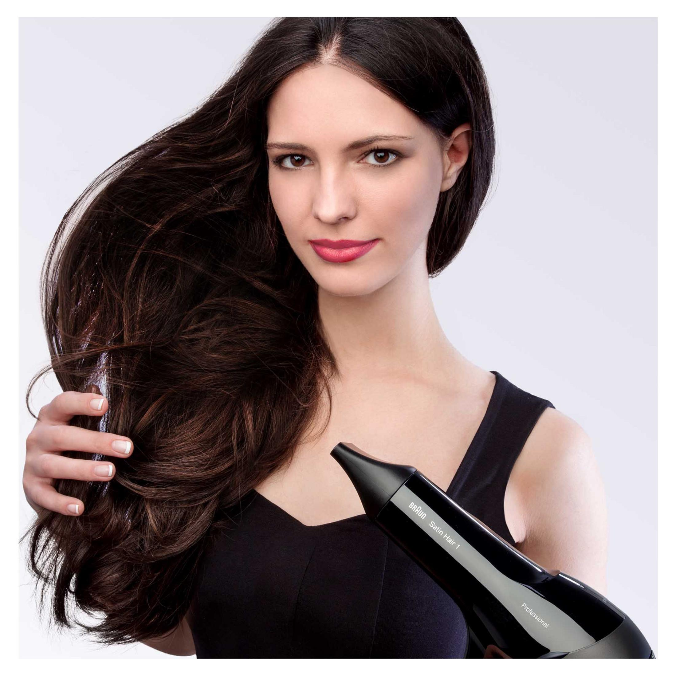 Una donna con lunghi capelli scuri che tiene un asciugacapelli nero, sorridendo.