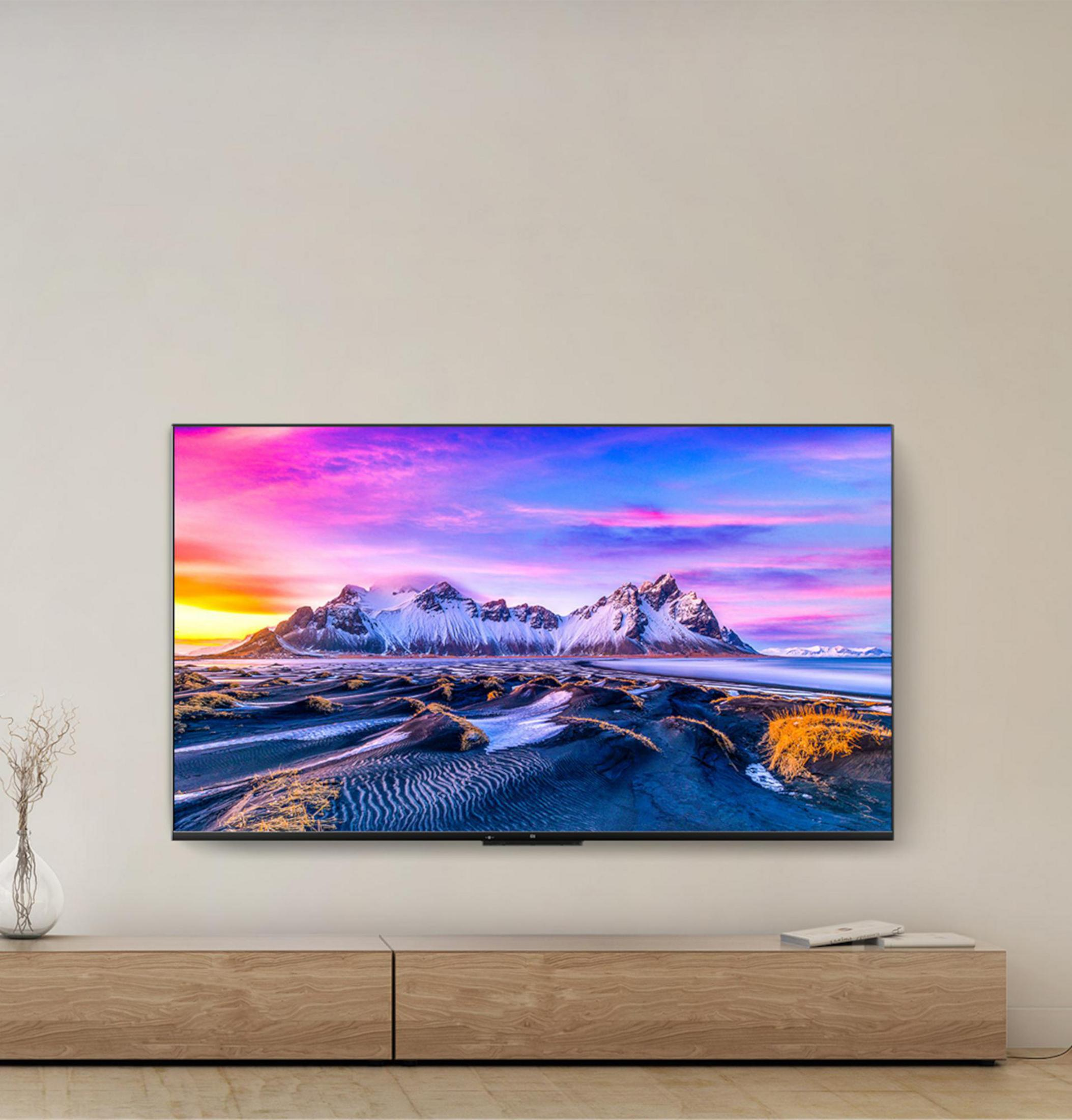 Un televisor muestra un paisaje montañoso escénico. El televisor está sobre un soporte de madera. El fondo es una pared crema.