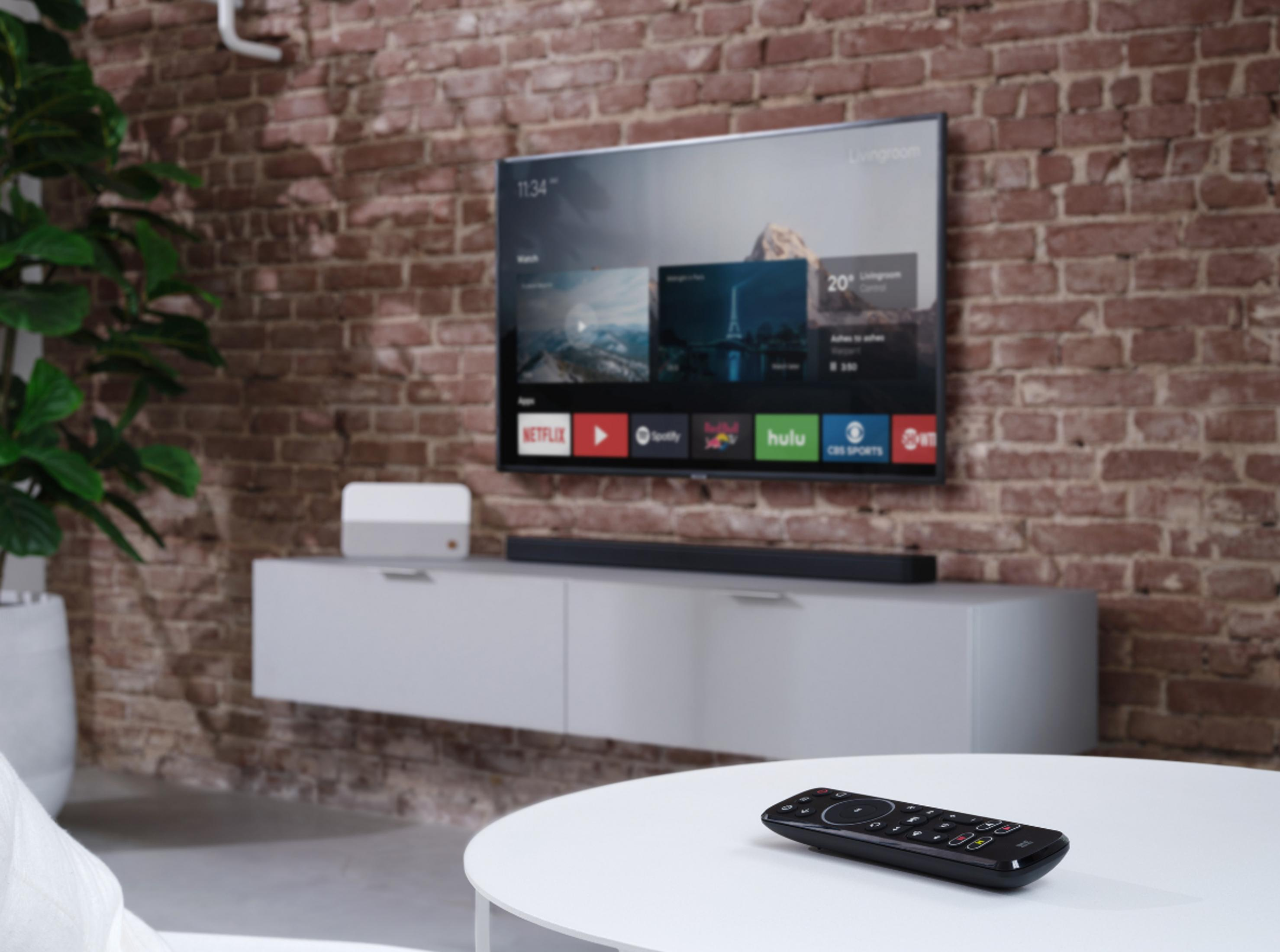Una sala de estar moderna con un televisor montado en una pared de ladrillo sobre una consola blanca. Un mando a distancia descansa sobre una mesa blanca.