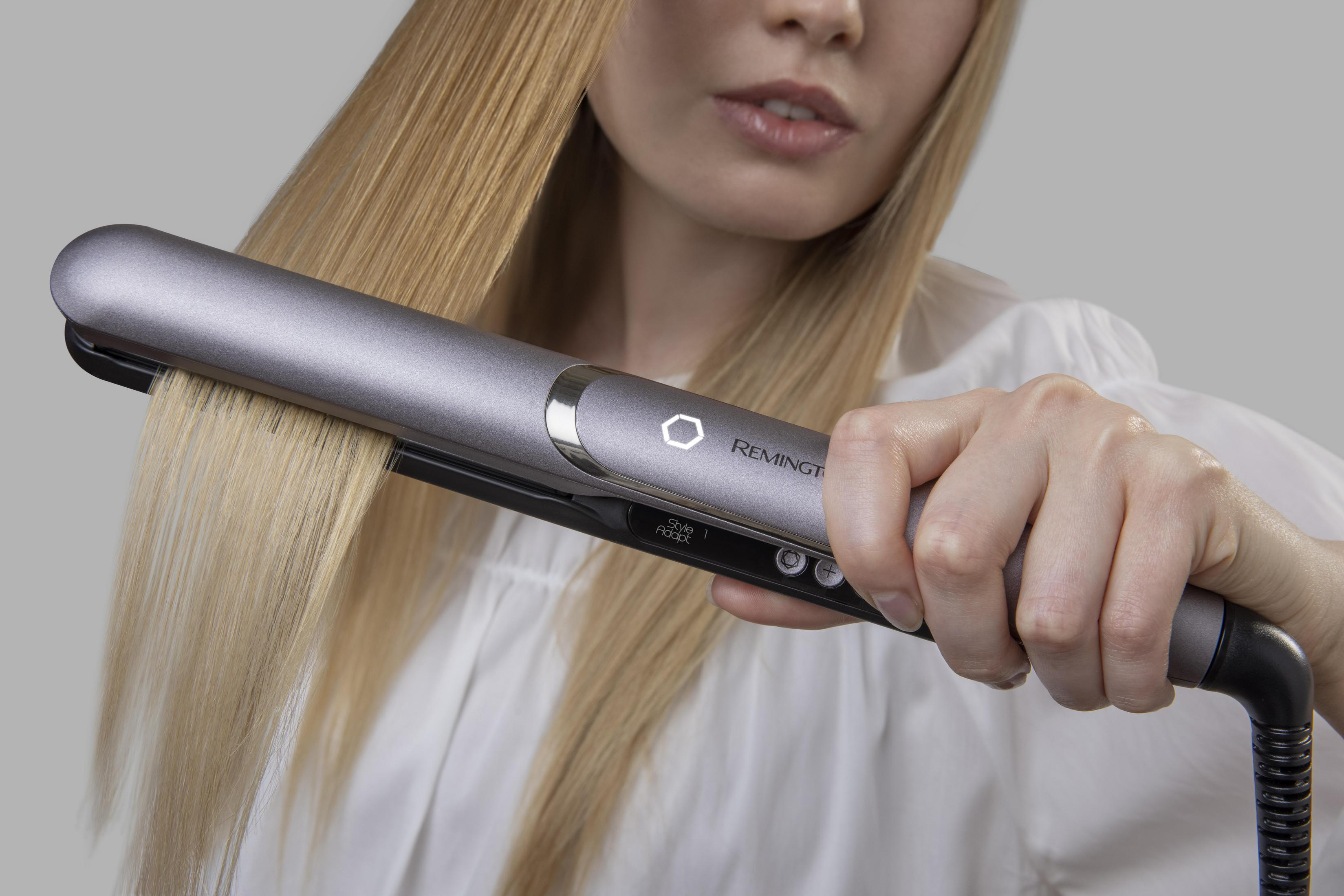 Una donna usa una piastra per capelli sui suoi capelli biondi, ripresa ravvicinata.