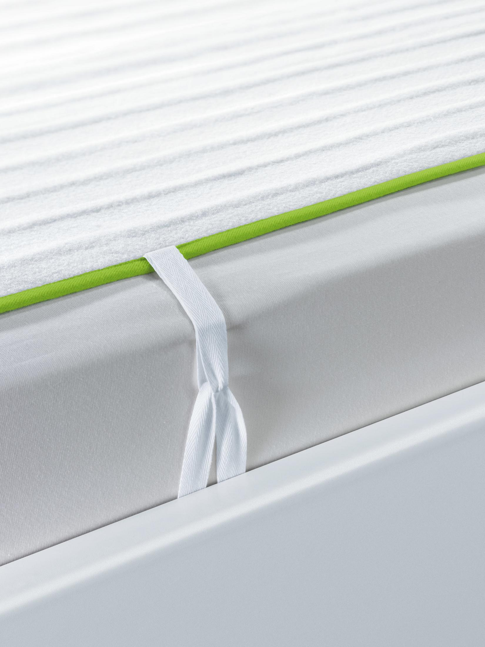 Primer plano de un protector de colchón blanco con ribete verde y correas blancas.