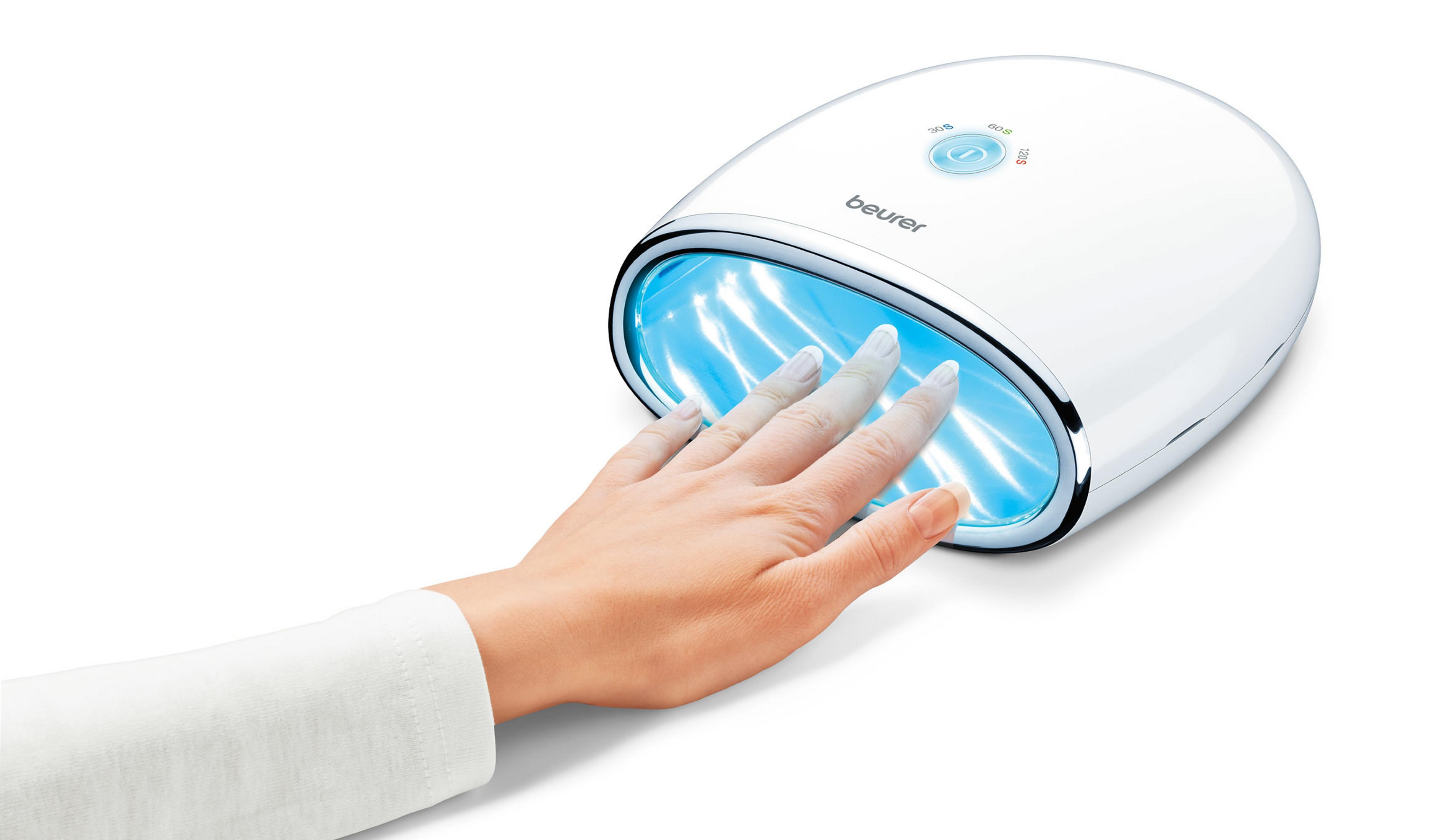 Hand mit Nägeln unter einem weißen UV-Nageltrockner. Der Trockner ist weiß und hat blaues Licht.