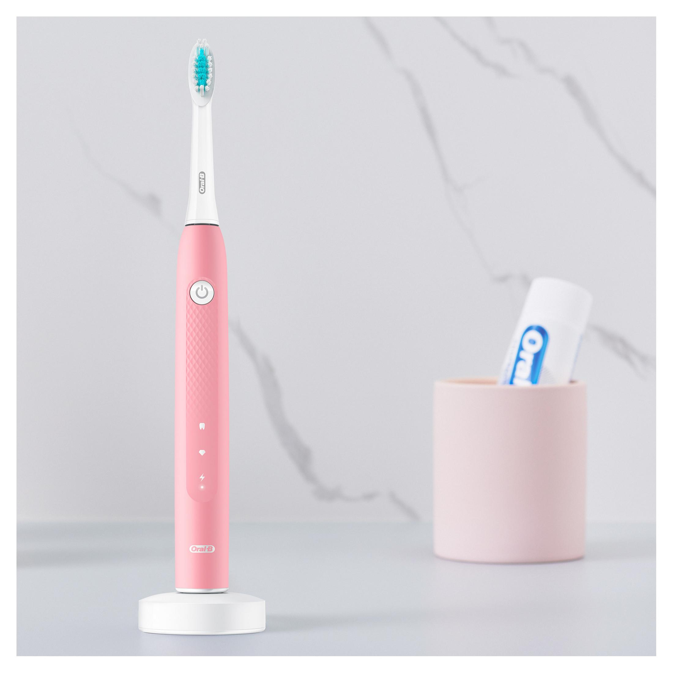 Cepillo de dientes eléctrico rosa y pasta de dientes en una taza rosa sobre una superficie blanca. Fondo blanco.