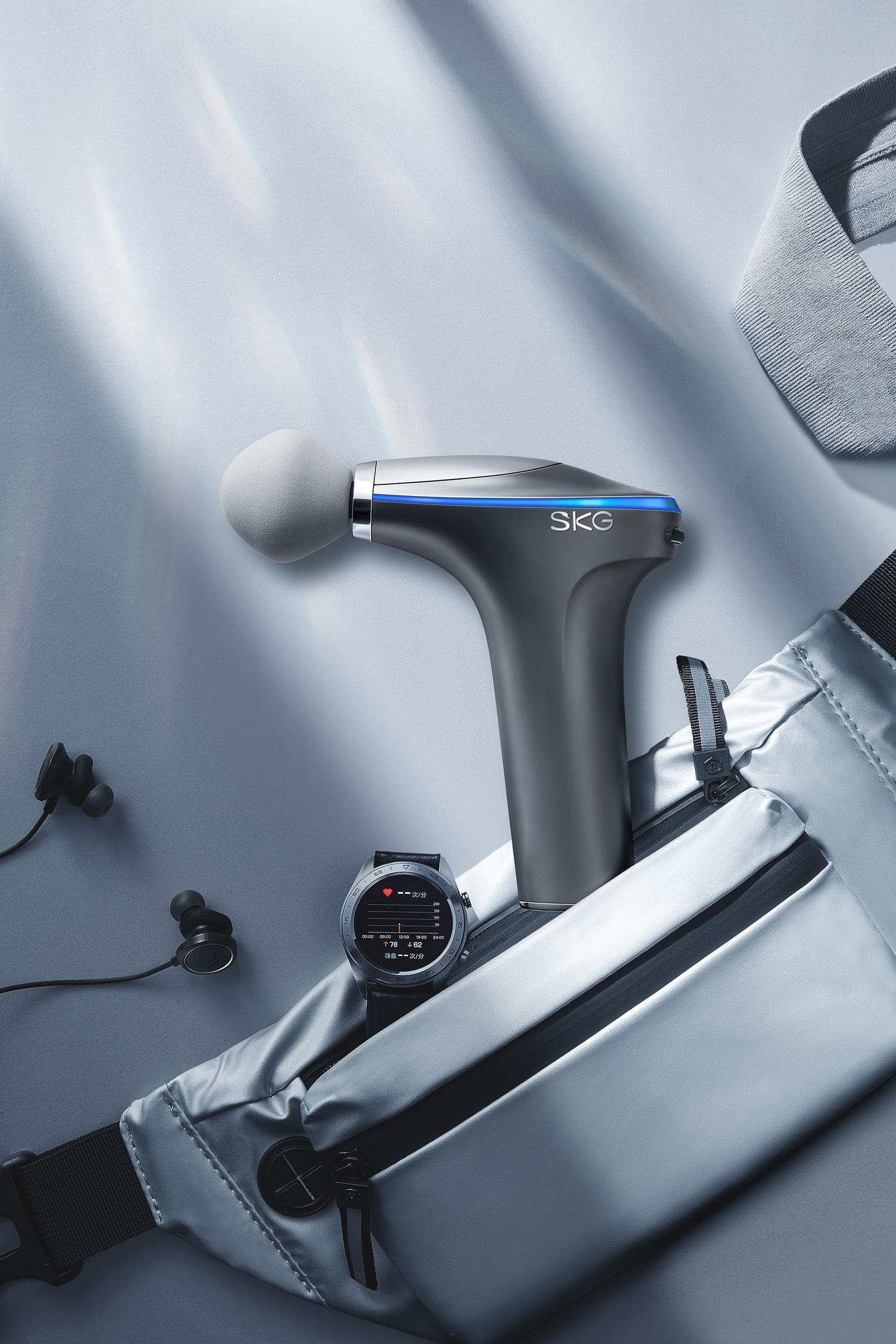 Eine Massagepistole, eine Smartwatch und andere Gegenstände auf hellblauem Untergrund.