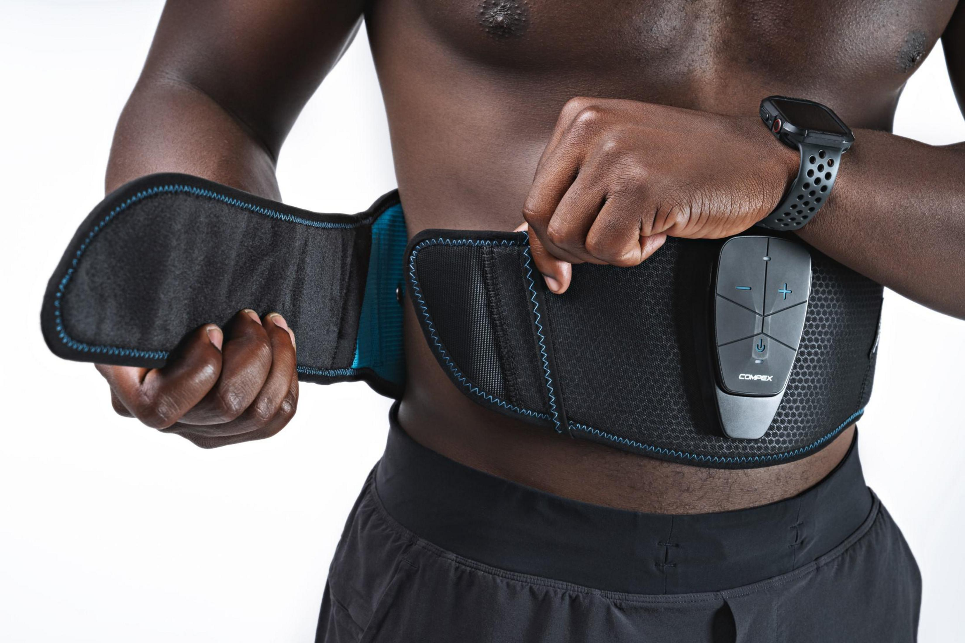 Mann trägt schwarzen Gürtel mit einem Compex-Gerät. Weißer Hintergrund. Schwarze Shorts.