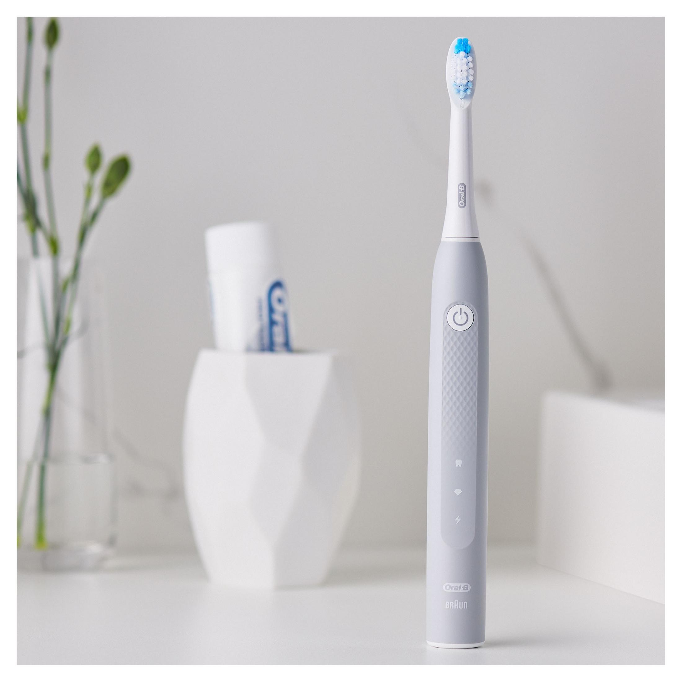 Spazzolino elettrico e dentifricio in un vaso bianco. Lo spazzolino è grigio e bianco. Sfondo pulito.