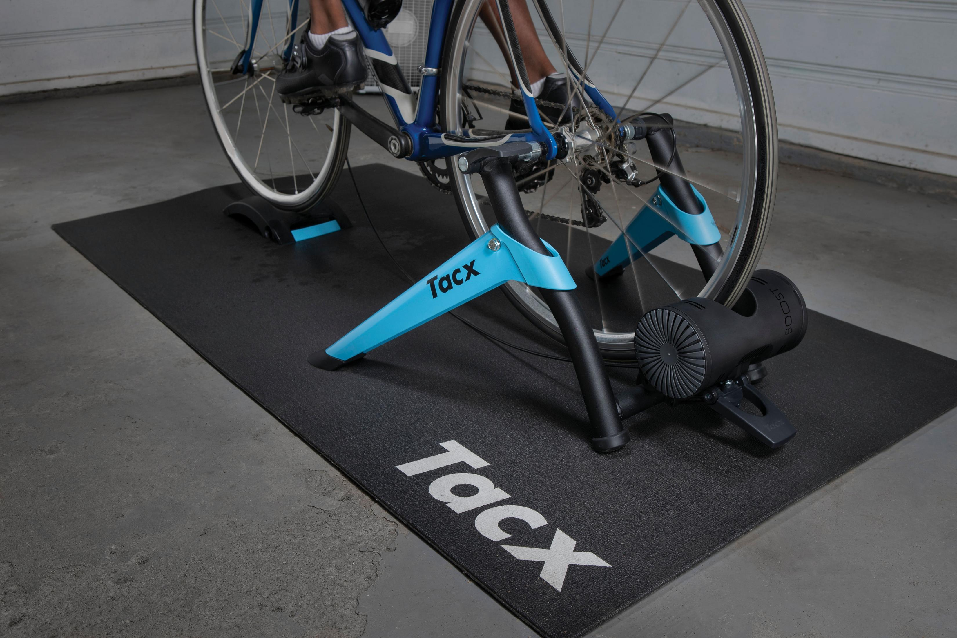 Heimtrainer auf schwarzer Matte, mit blauen Stützen und Tacx-Logo.