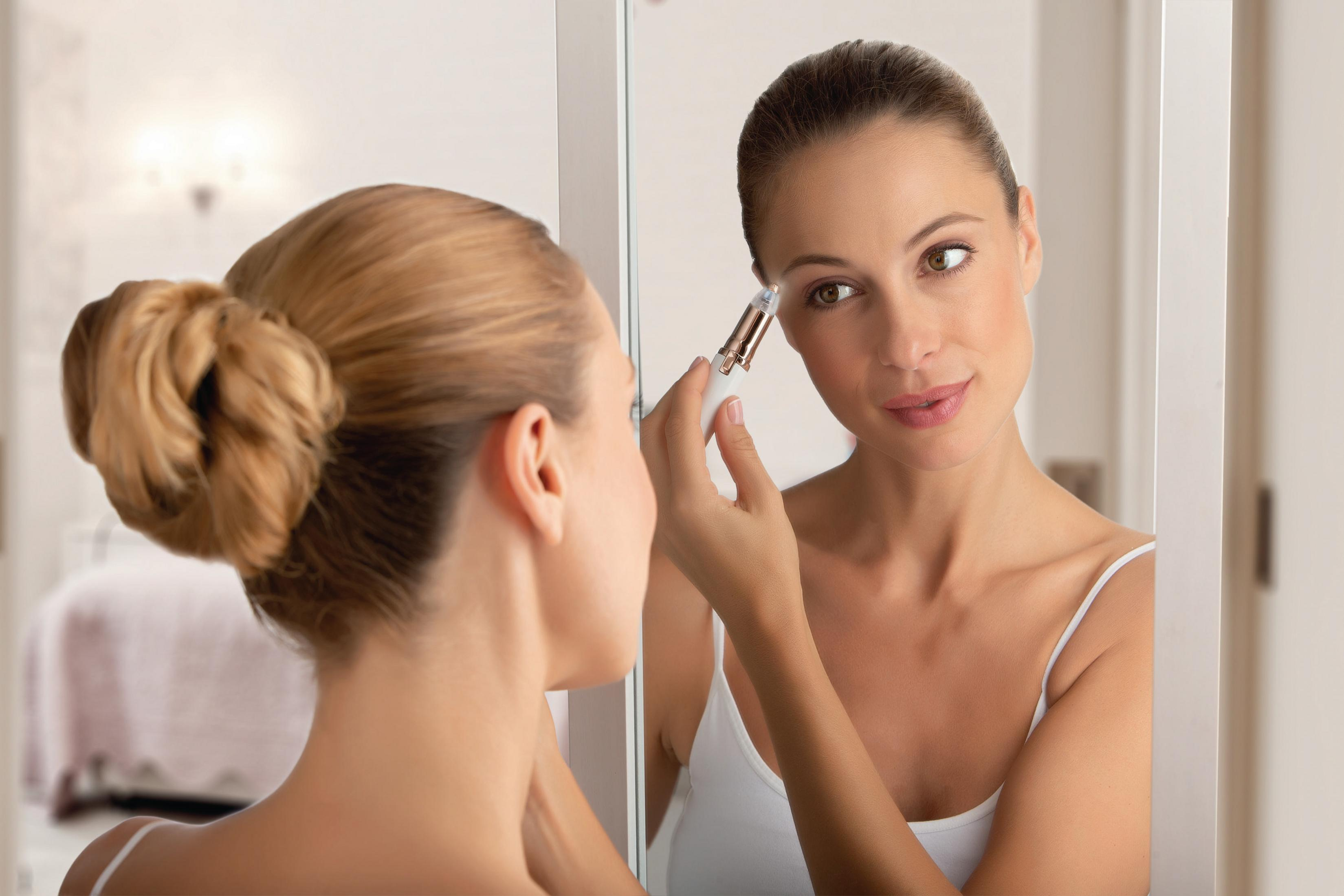 Donna allo specchio che applica il trucco con un dispositivo elettrico.