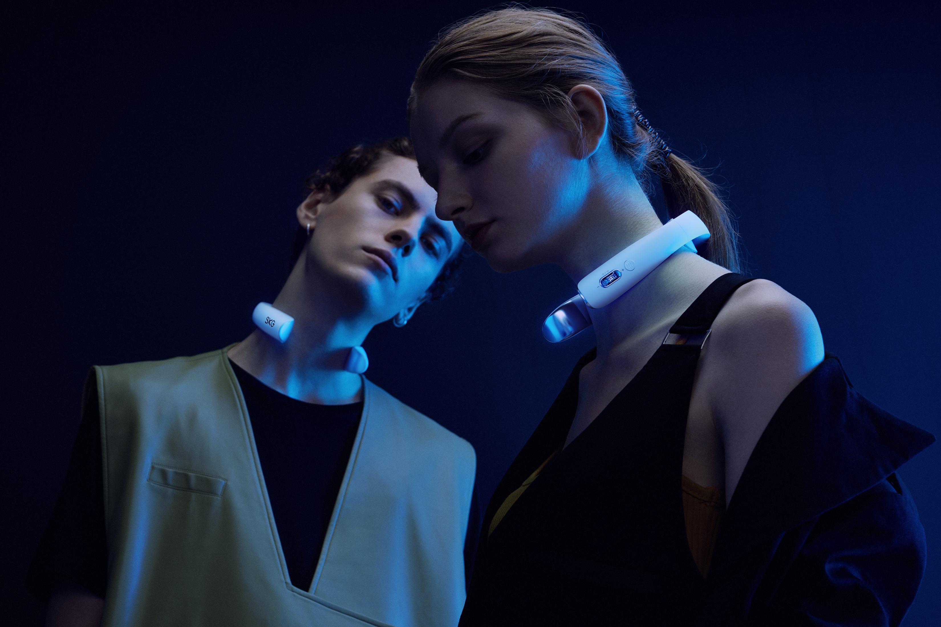 Un uomo e una donna con dispositivi LED al collo, su sfondo blu scuro.
