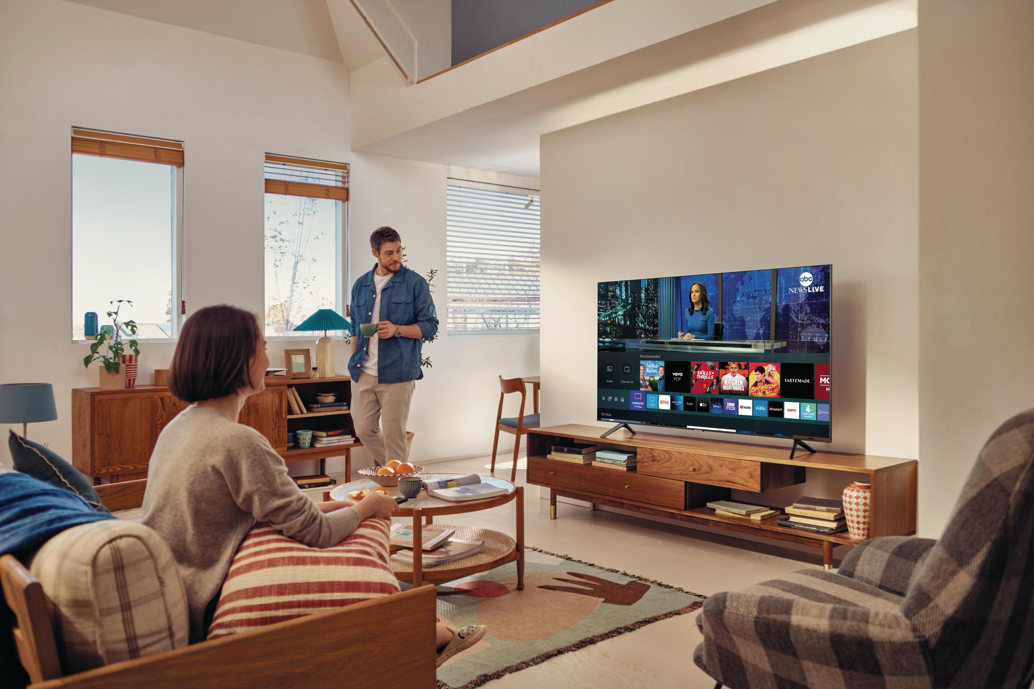 Salon z telewizorem pokazującym wiadomości, mężczyzna i kobieta, drewniane meble.