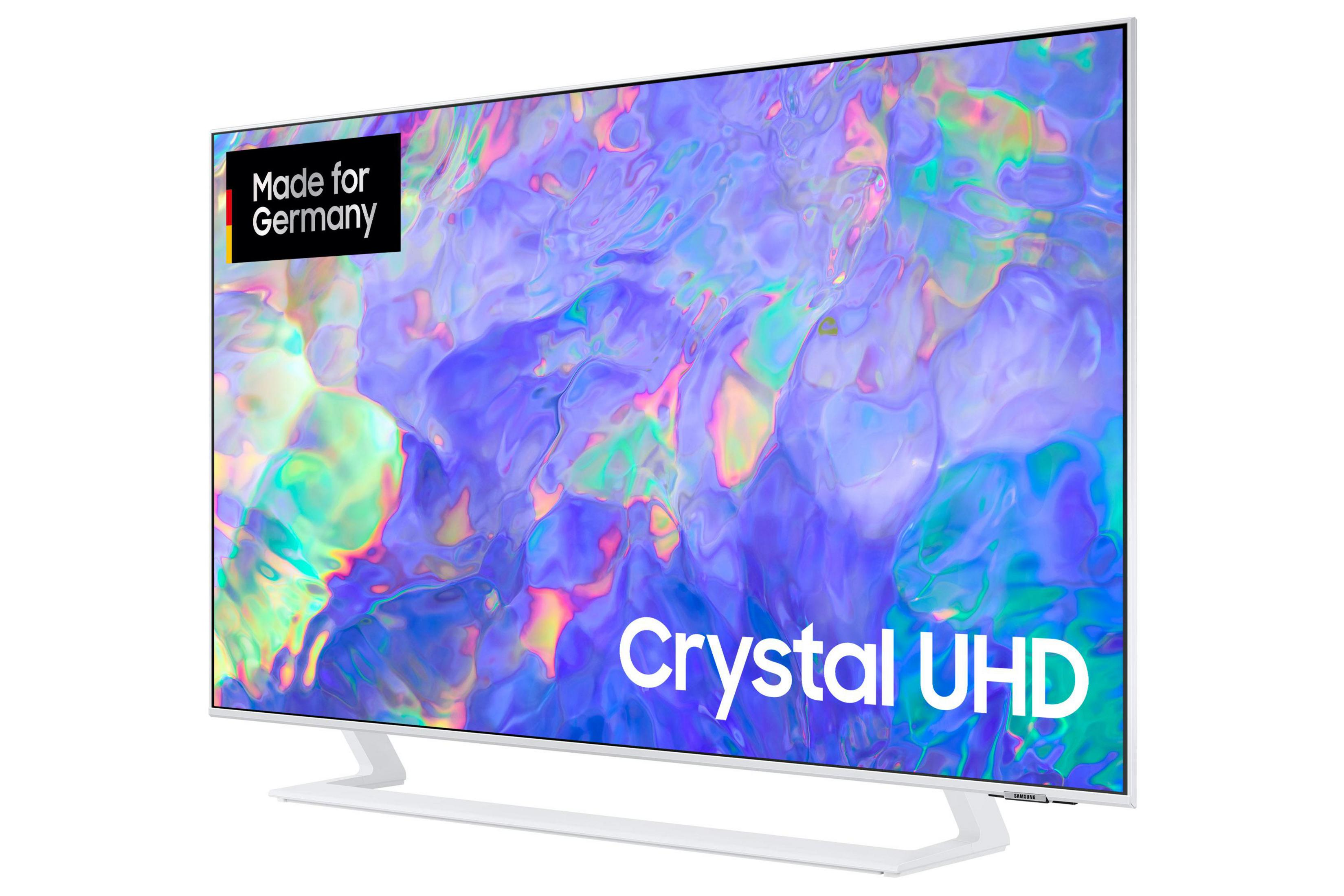 Biały telewizor z tekstem Crystal UHD i etykietą Made for Germany, pokazujący kolorową sztukę abstrakcyjną.