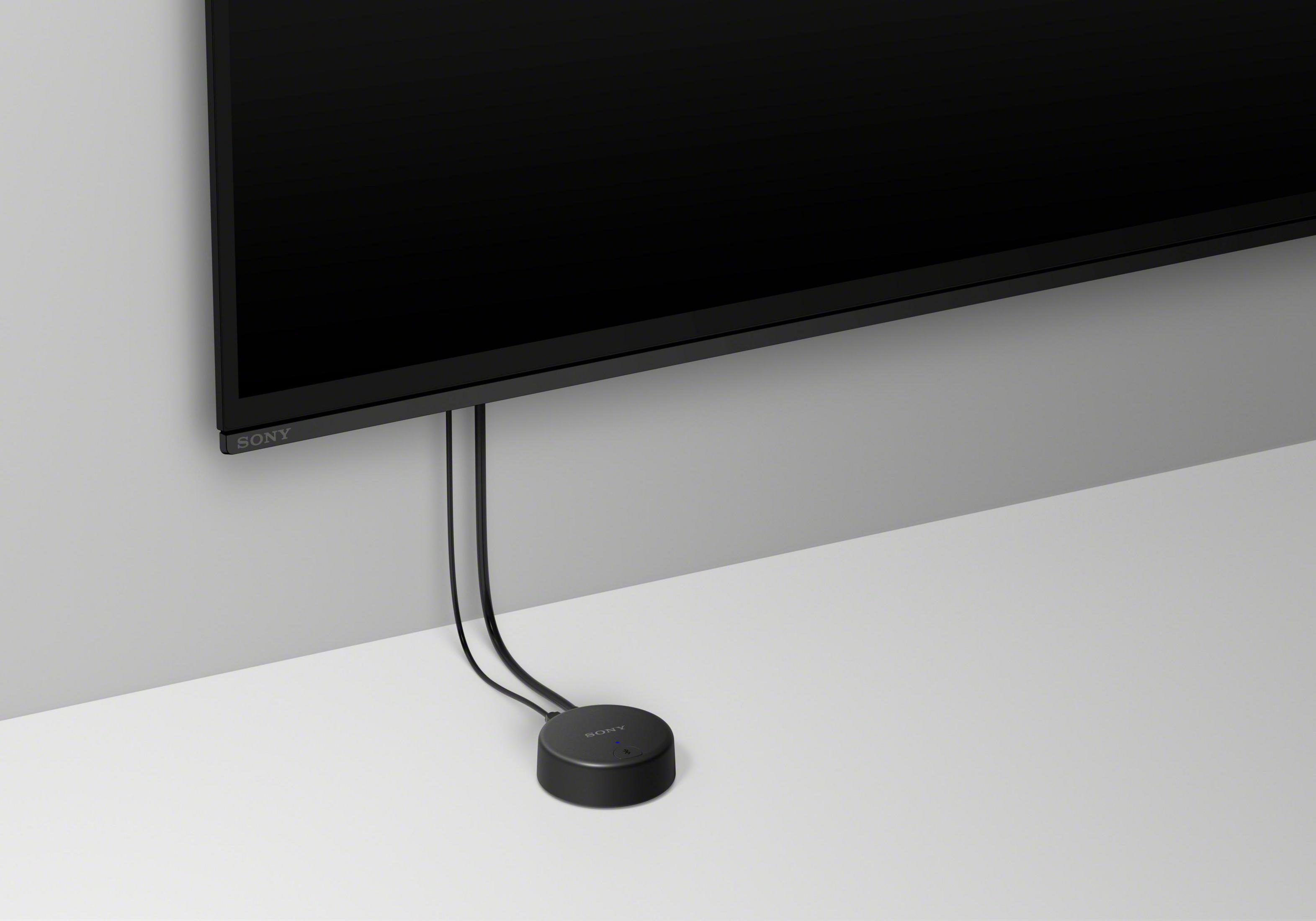 Un dispositivo negro y redondo conectado a un televisor. El televisor está montado en una pared blanca.
