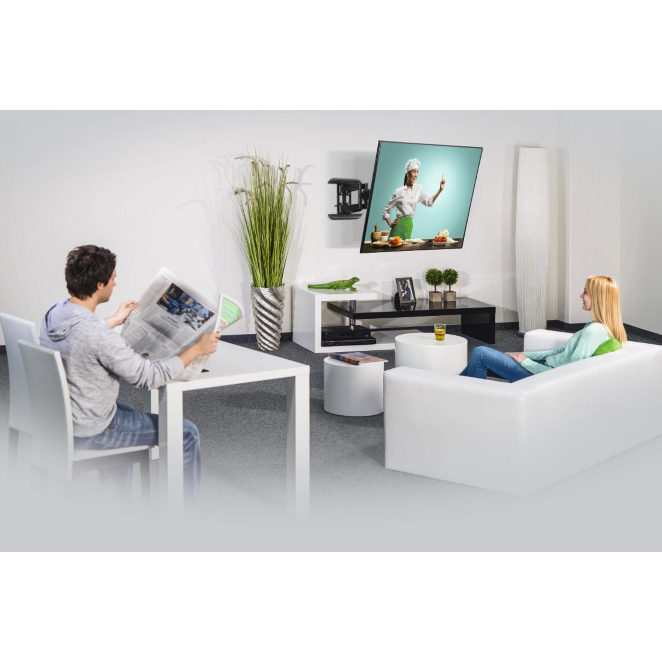 Wohnzimmer mit an der Wand montiertem Fernseher. Zwei Personen, Sofa, Couchtisch und Dekoration zu sehen.