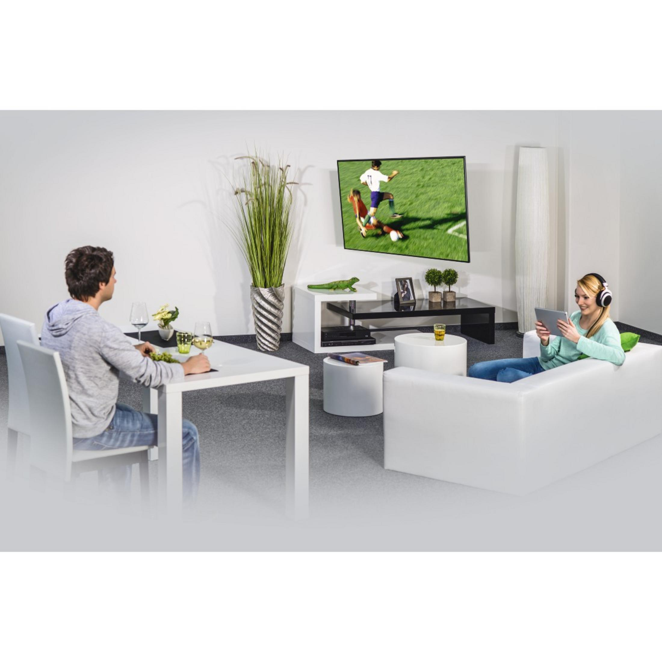Ein Wohnzimmer mit Fernseher an der Wand. Personen sitzen und benutzen Geräte.