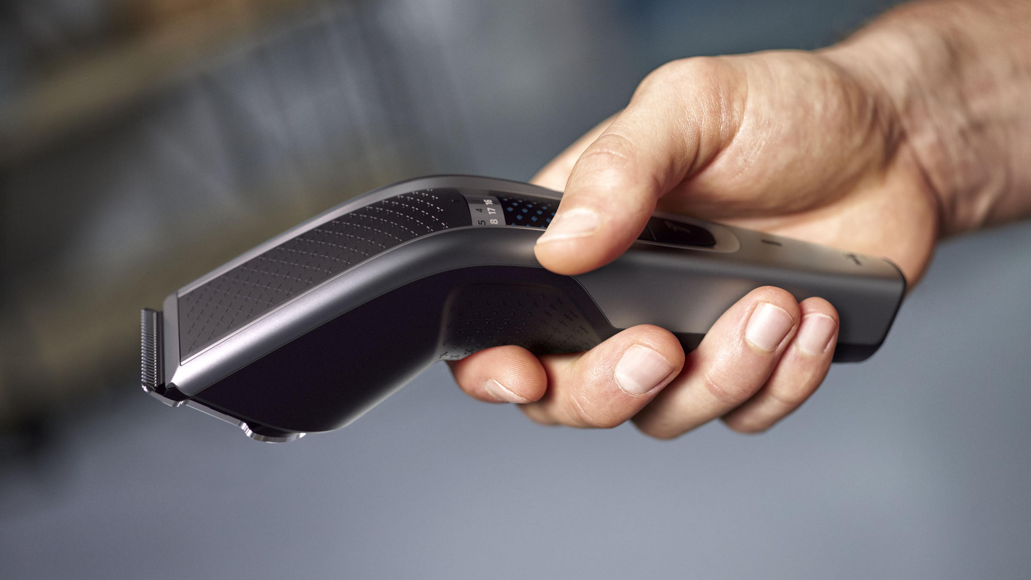 Dłoń trzymająca czarną maszynkę do włosów, gotową do użycia, z rozmytym tłem.