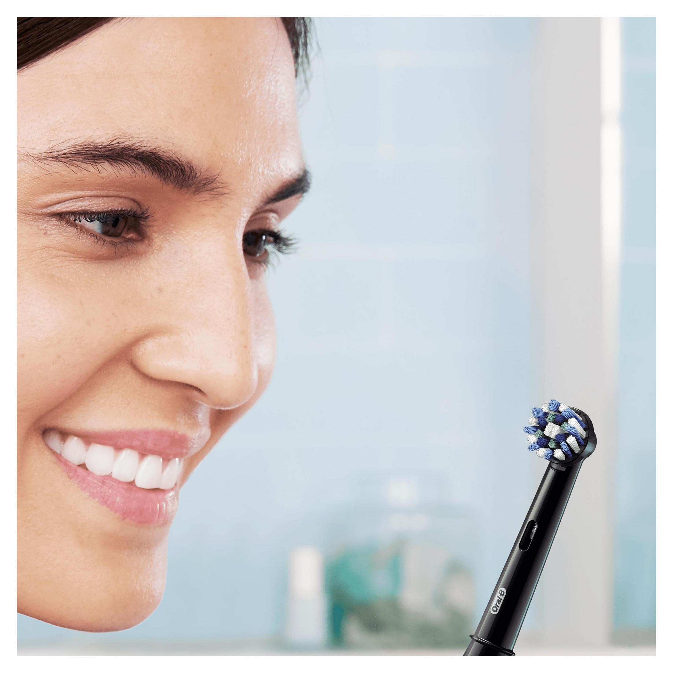 Mujer sonriendo, mirando un cabezal de cepillo de dientes eléctrico negro con cerdas azules y blancas.