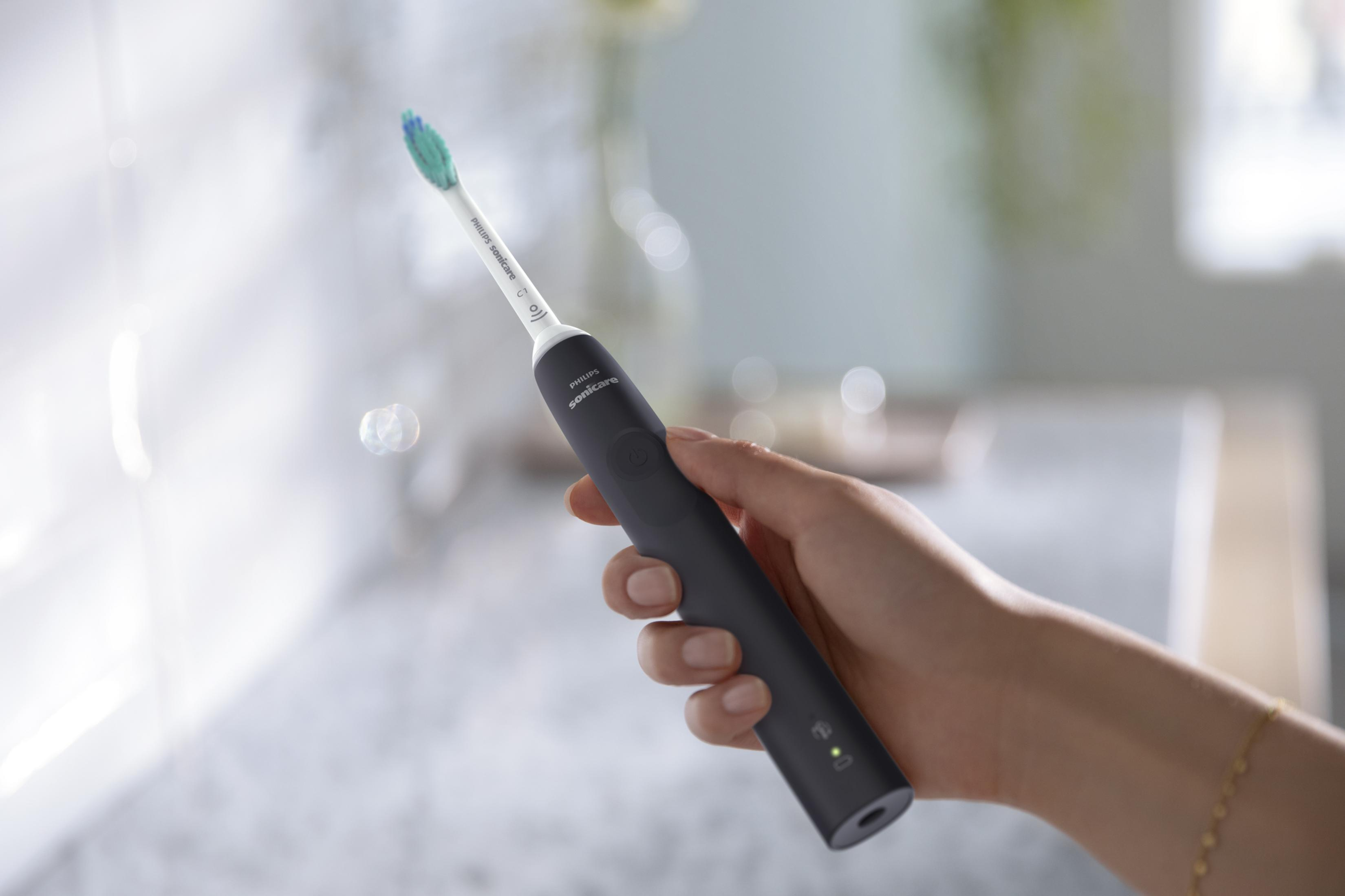 Dłoń trzymająca czarną elektryczną szczoteczkę do zębów Philips Sonicare z zielonym światłem.