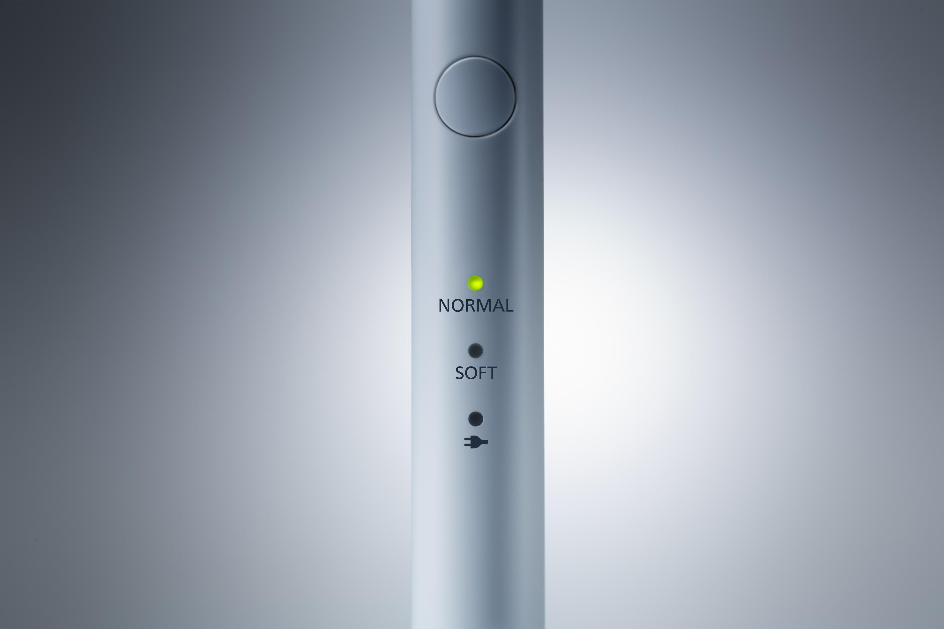 Zbliżenie elektrycznej szczoteczki do zębów z trybami Normalny i Miękki wskazywanymi przez światła.