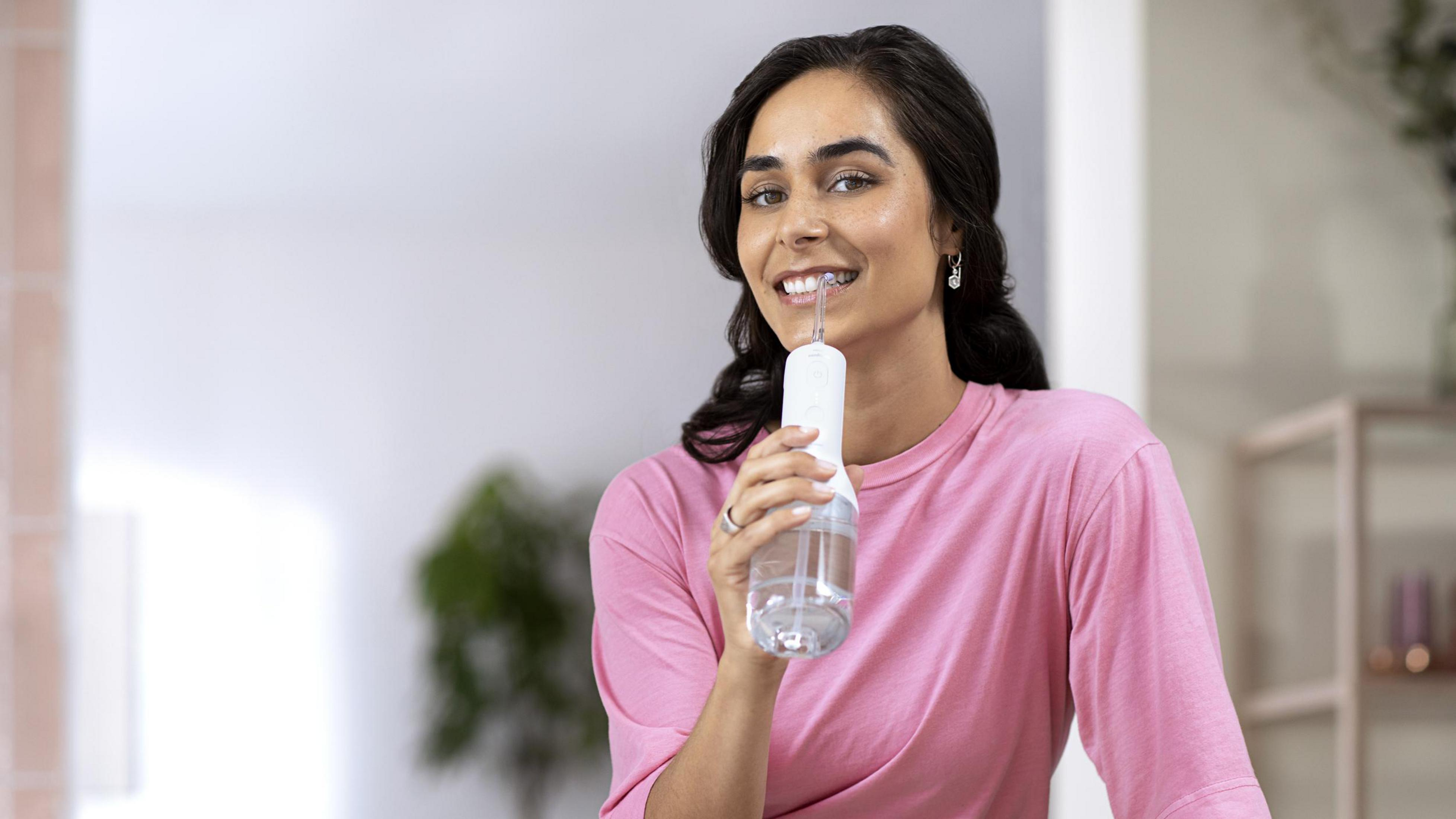 Una donna che usa un idropulsore, sorridendo alla fotocamera, tenendo il dispositivo vicino alla bocca.