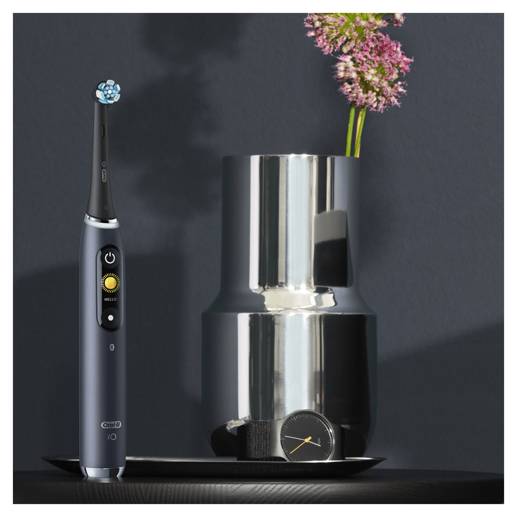 Elektrische Zahnbürste und Zubehör auf dunkler Oberfläche. Blume und Vase im Hintergrund.