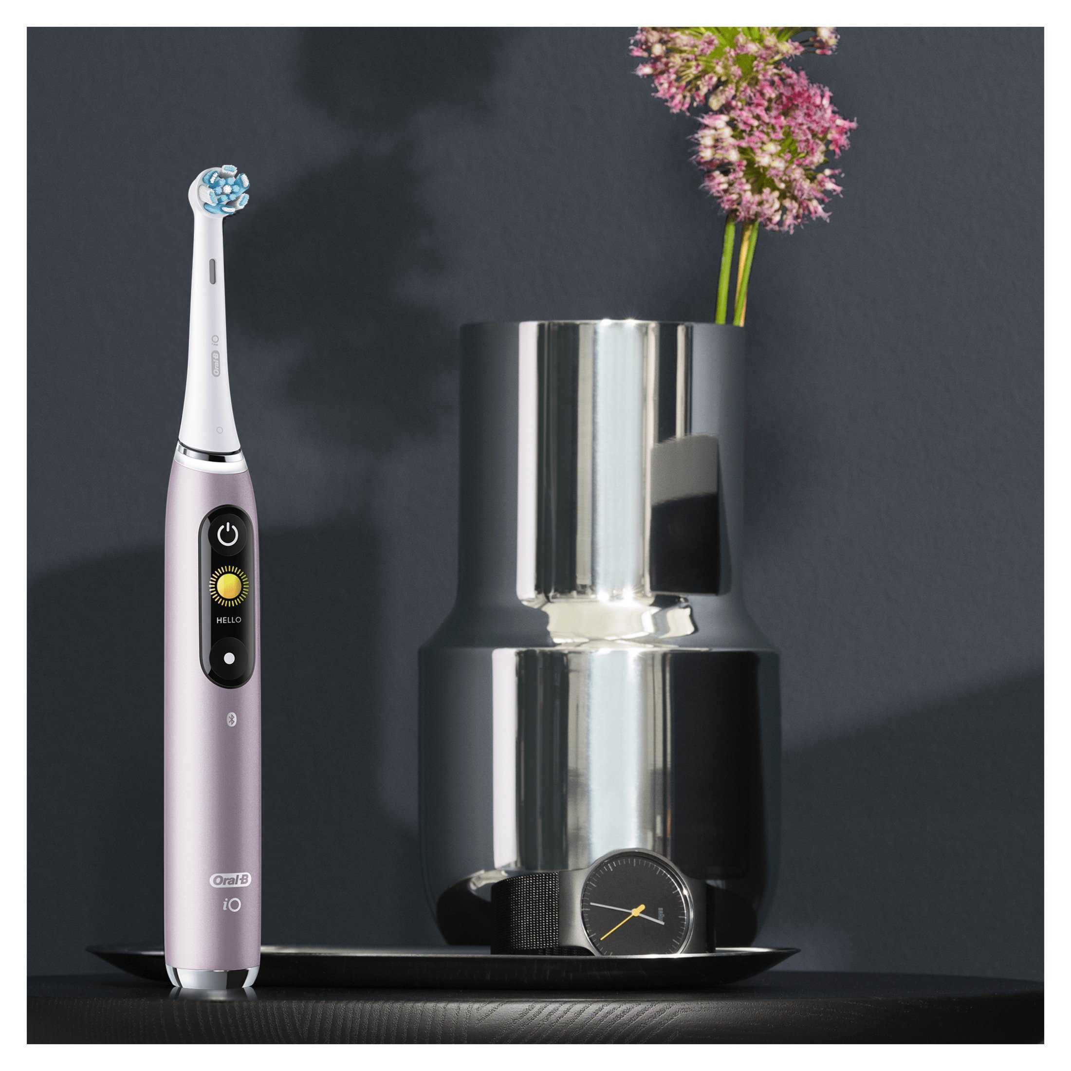 Uno spazzolino elettrico rosa con display, vicino a un vaso con fiori.