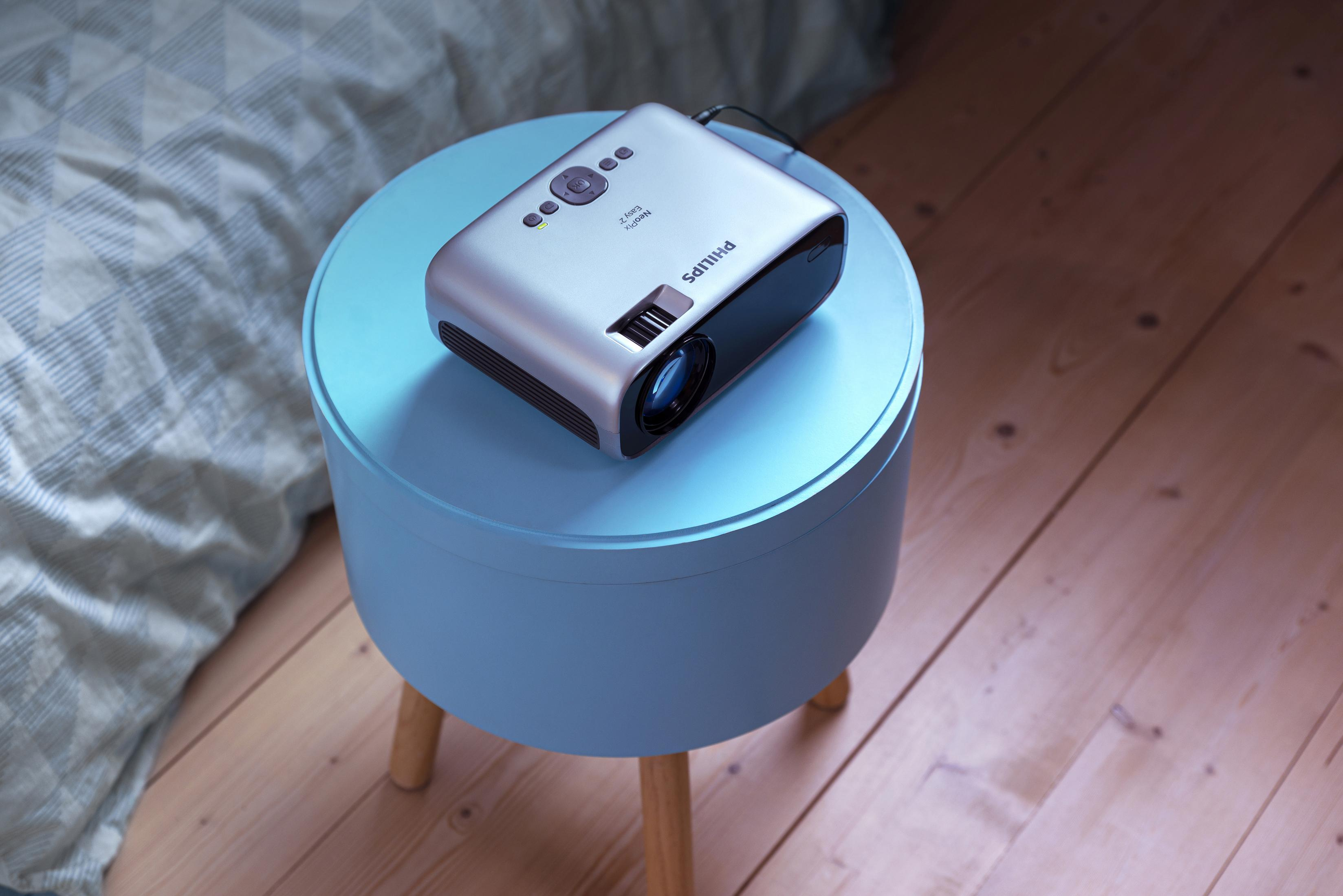 Srebrny projektor Philips na niebieskim stole w pokoju.