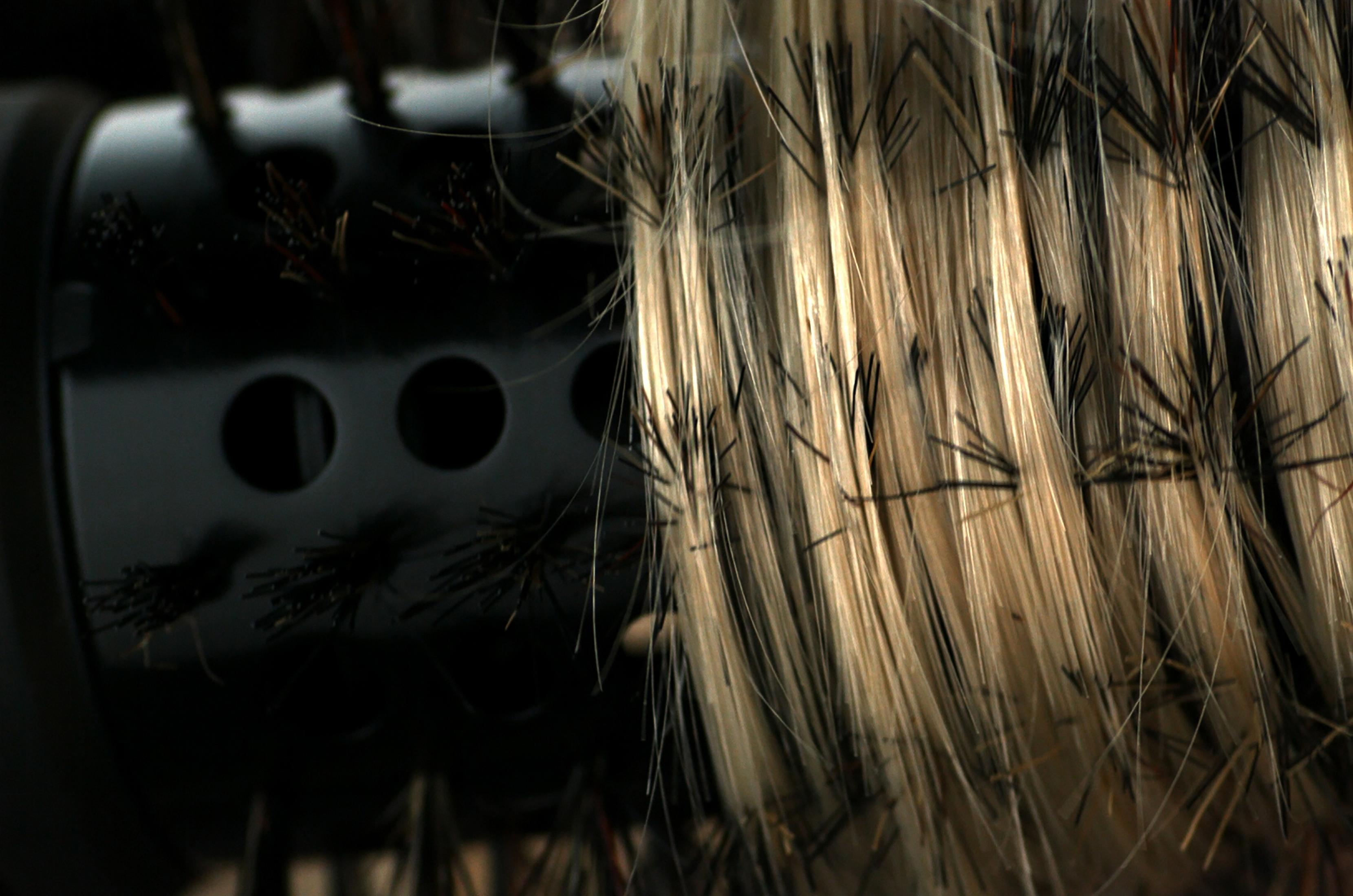 Zbliżenie szczotki do suszarki do włosów z blond pasmami.