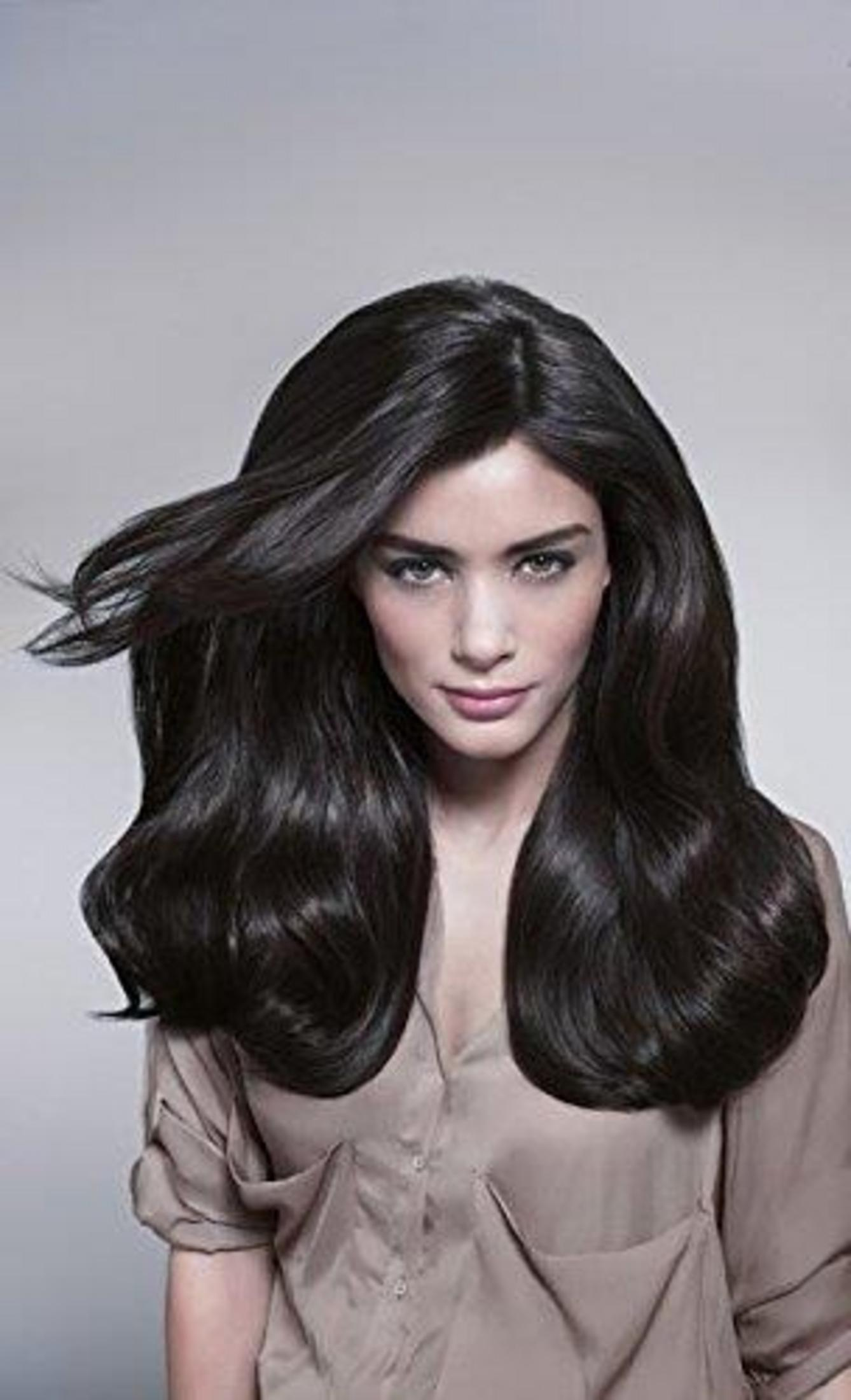 Giovane donna con lunghi capelli scuri e ondulati. Indossa una camicia marrone chiaro.