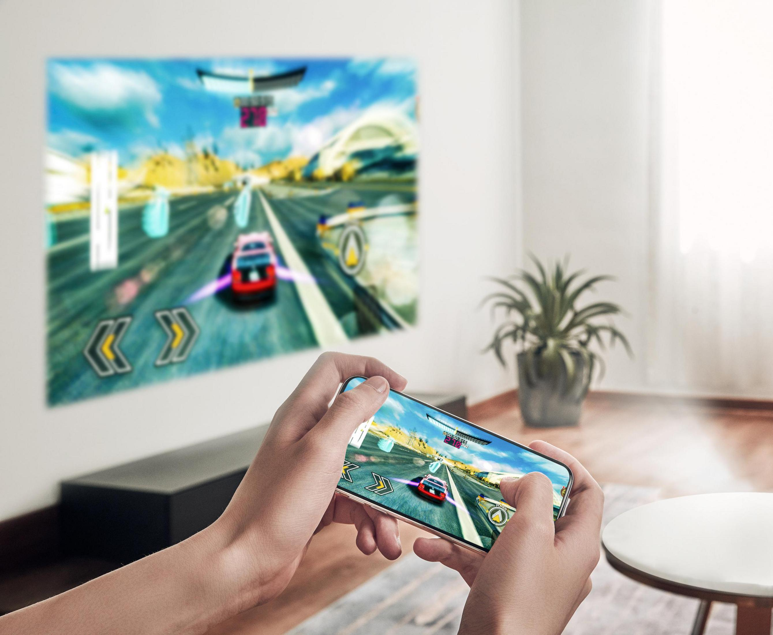 Manos sosteniendo un teléfono que muestra un juego de carreras con una imagen borrosa en la pared.