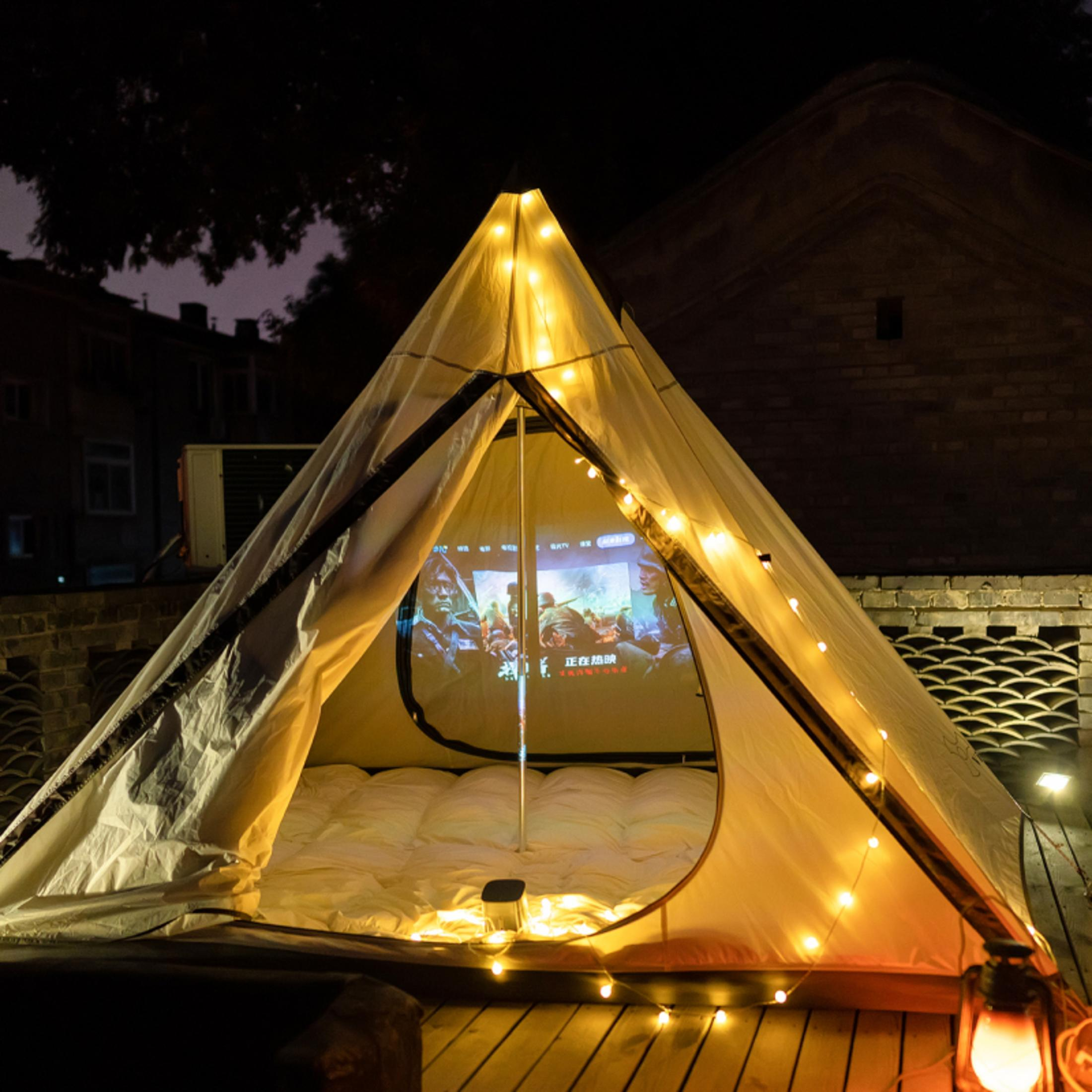 Beleuchtetes Zelt mit Leinwand, die Film zeigt, draußen nachts mit Lichterketten.