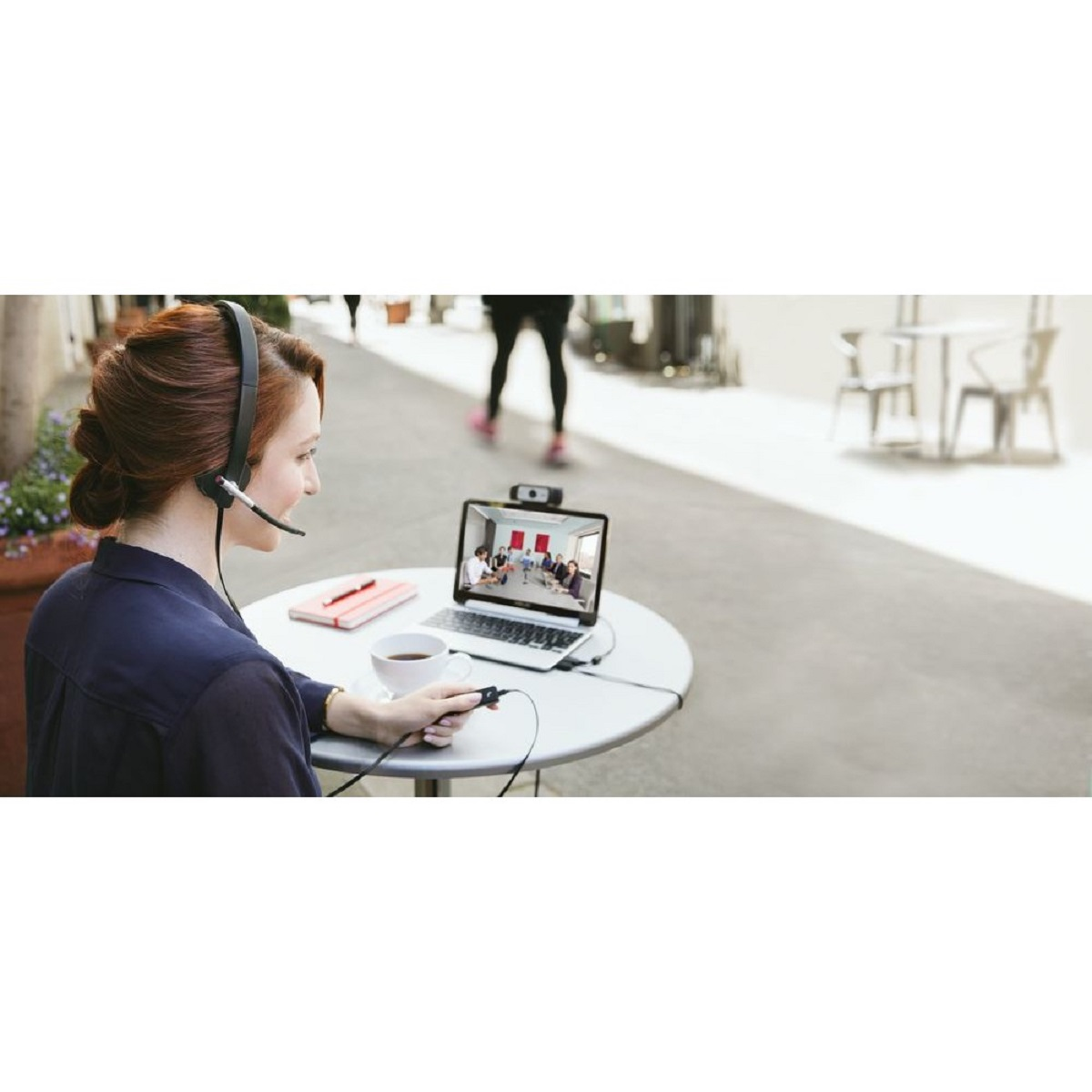 Kobieta podczas rozmowy wideo z zestawem słuchawkowym, siedząca przy stole z laptopem i filiżanką kawy.