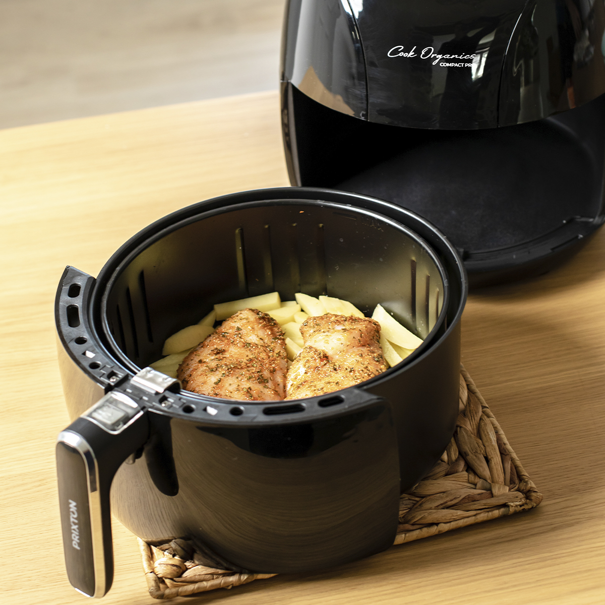 Freidora de aire con pollo y patatas en una mesa.