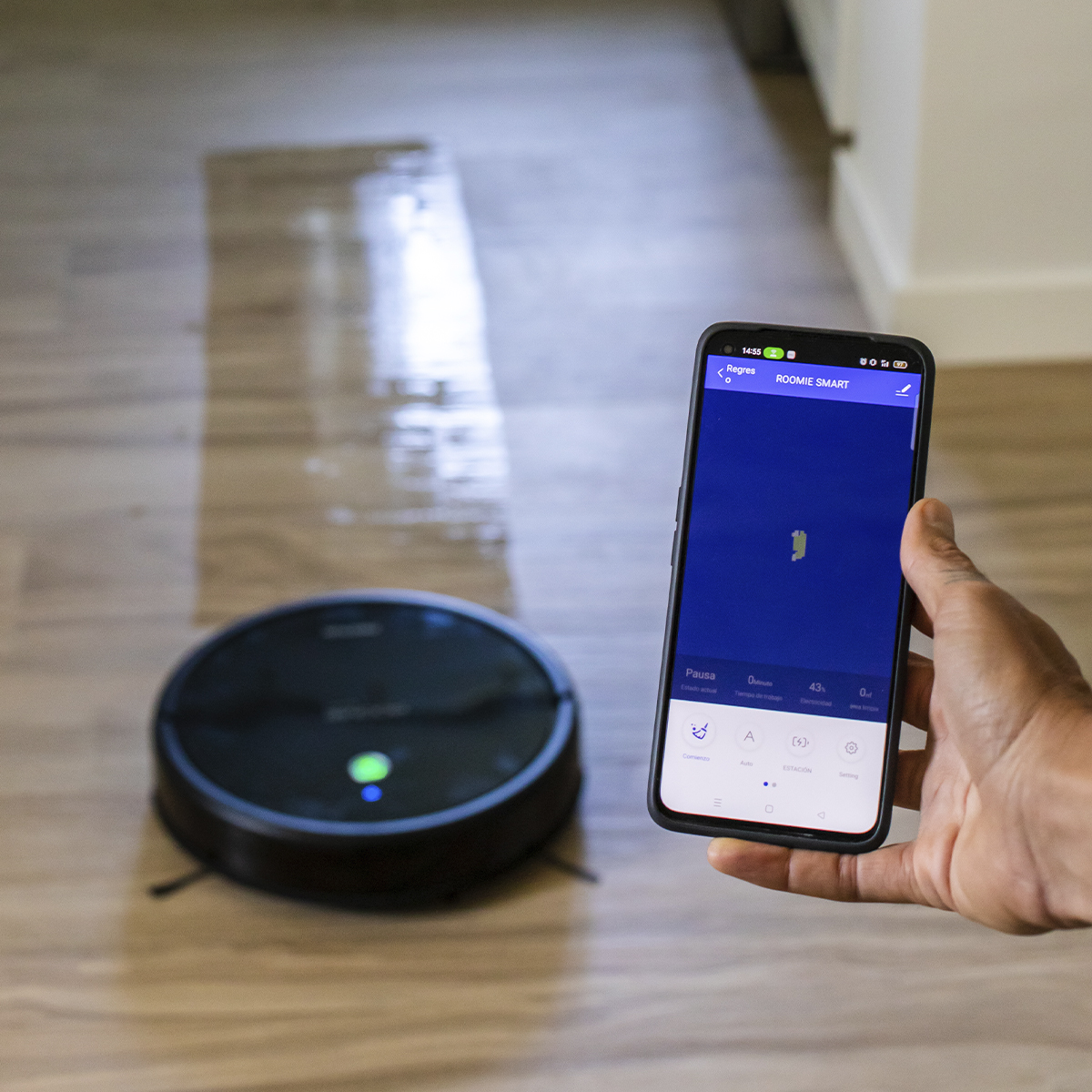 Dłoń trzymająca smartfona obok czarnego robota odkurzającego.