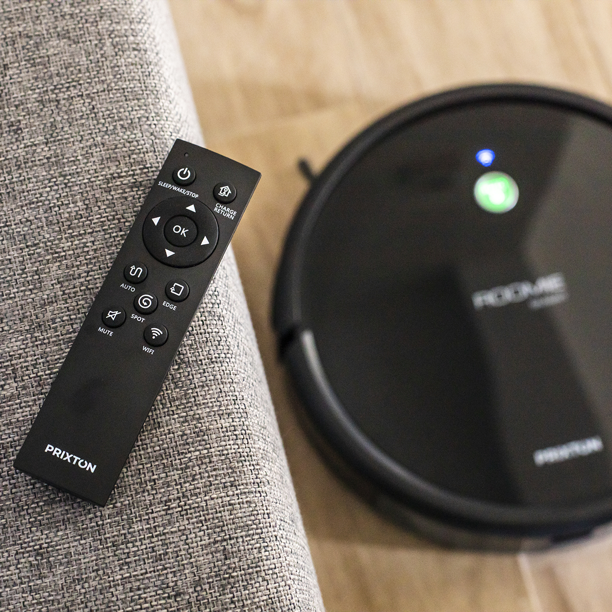 Czarny pilot i czarny odkurzacz robot. Oba są na szarej sofie.