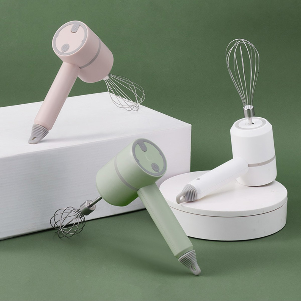 Drei kleine elektrische Schneebesen in Rosa, Grün und Weiß auf grüner und weißer Oberfläche.