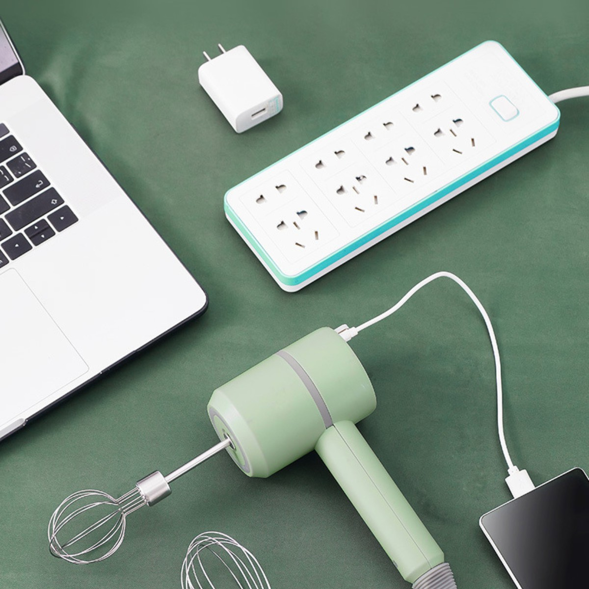 Ein Laptop, eine Steckdosenleiste und ein grüner Handmixer mit Ladegerät und Telefon. Verschiedene Geräte sind aktiv.