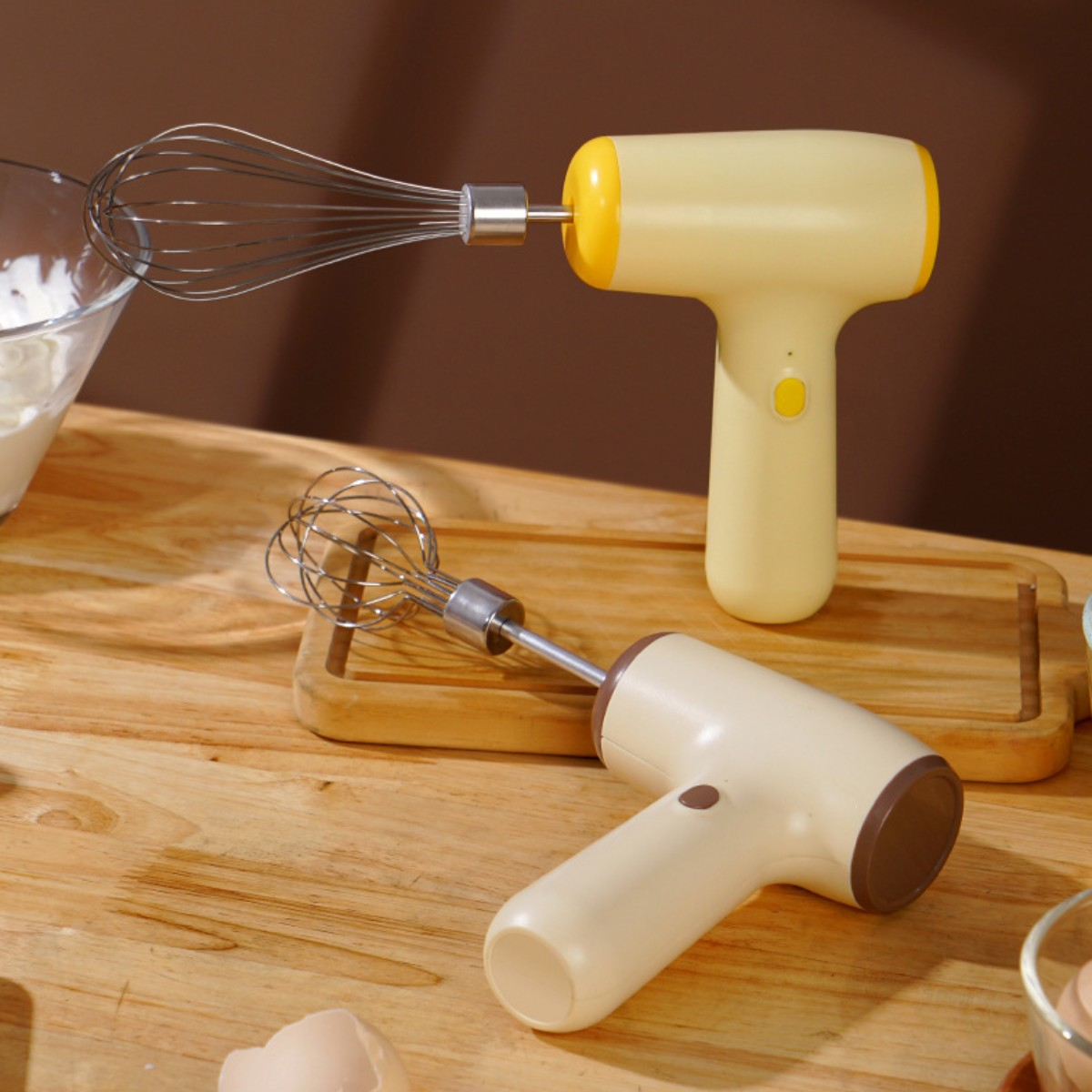 Zwei cremefarbene Handmixer mit Schneebesen und Quirl auf Holzoberfläche.
