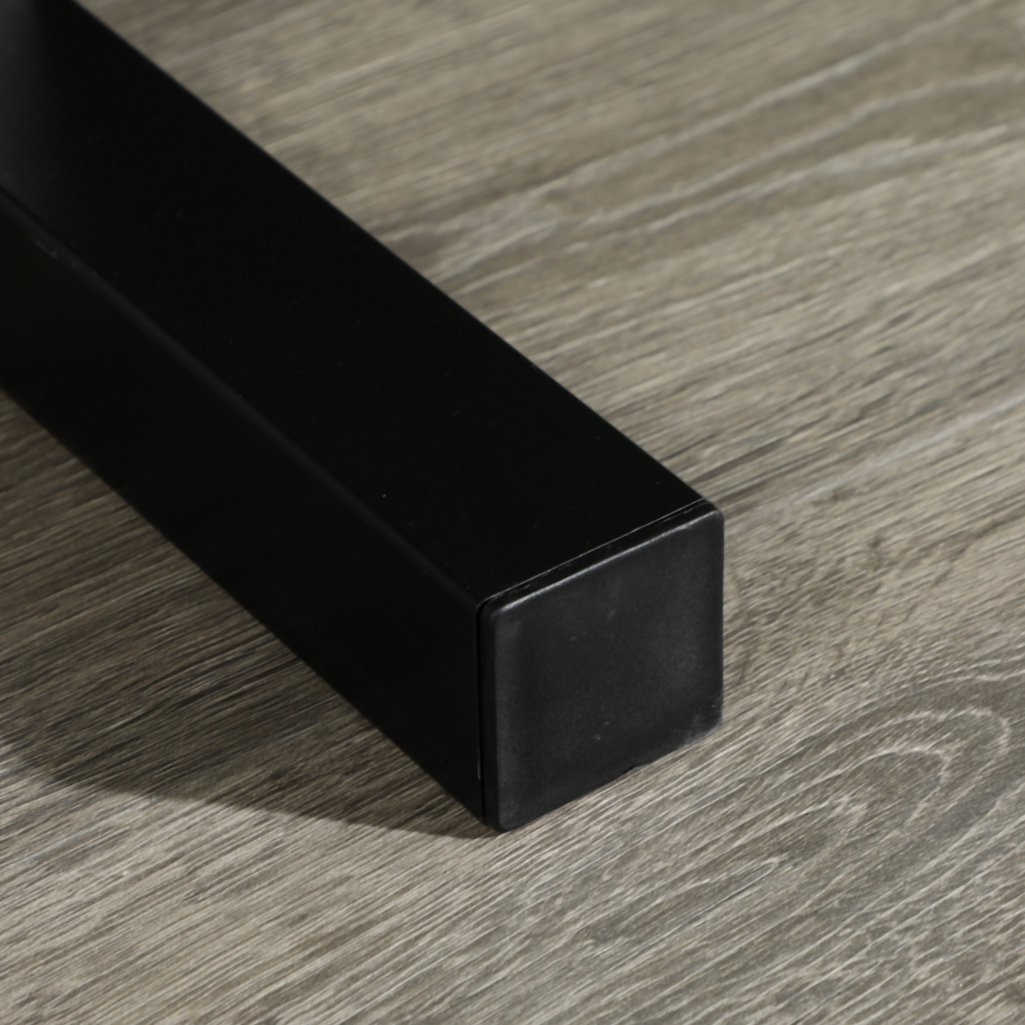 Primer plano de una pata de mesa de metal negro, sobre un suelo de madera.