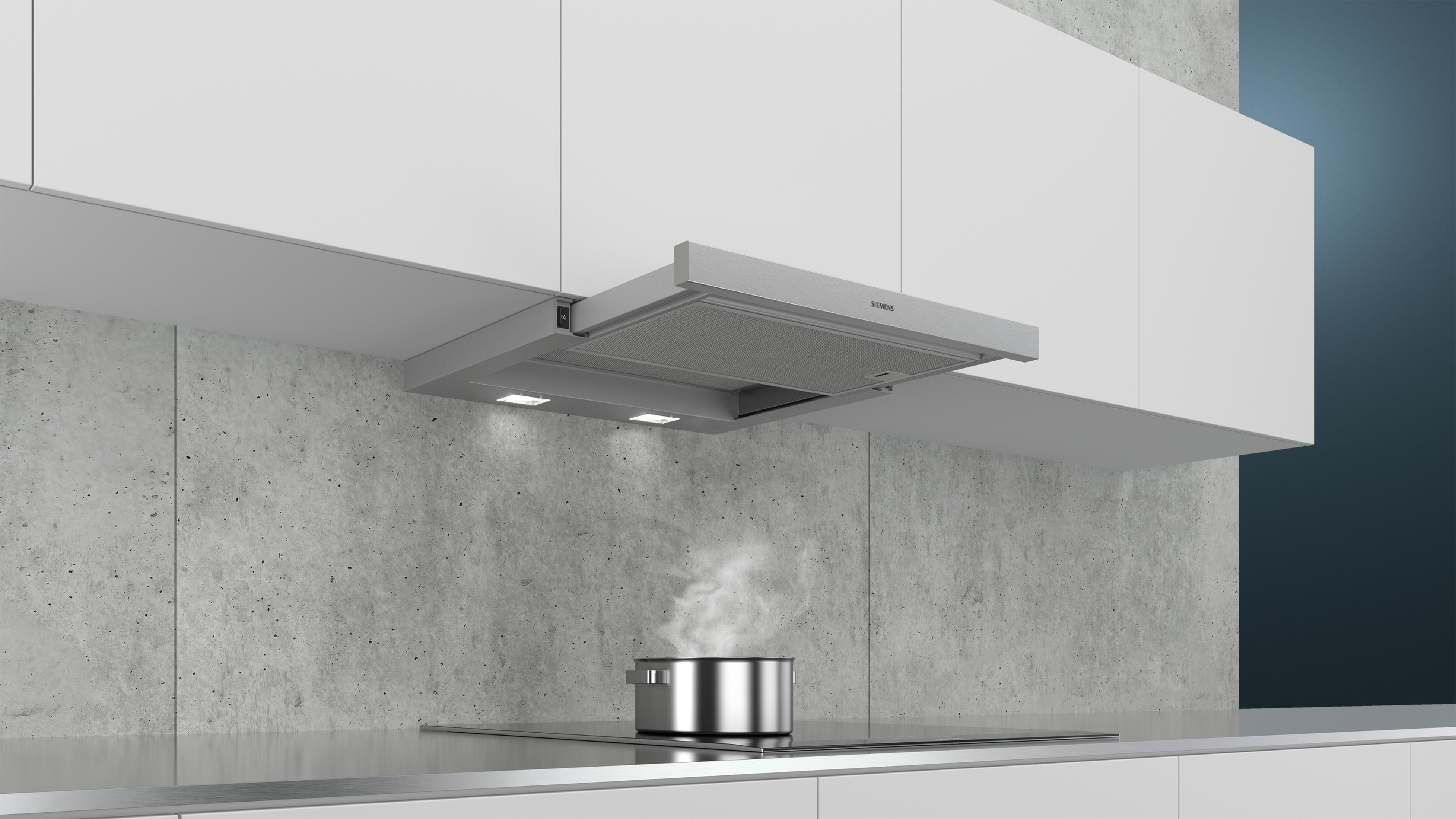 Okap ze stali nierdzewnej nad płytą grzejną z garnkiem parującego jedzenia.