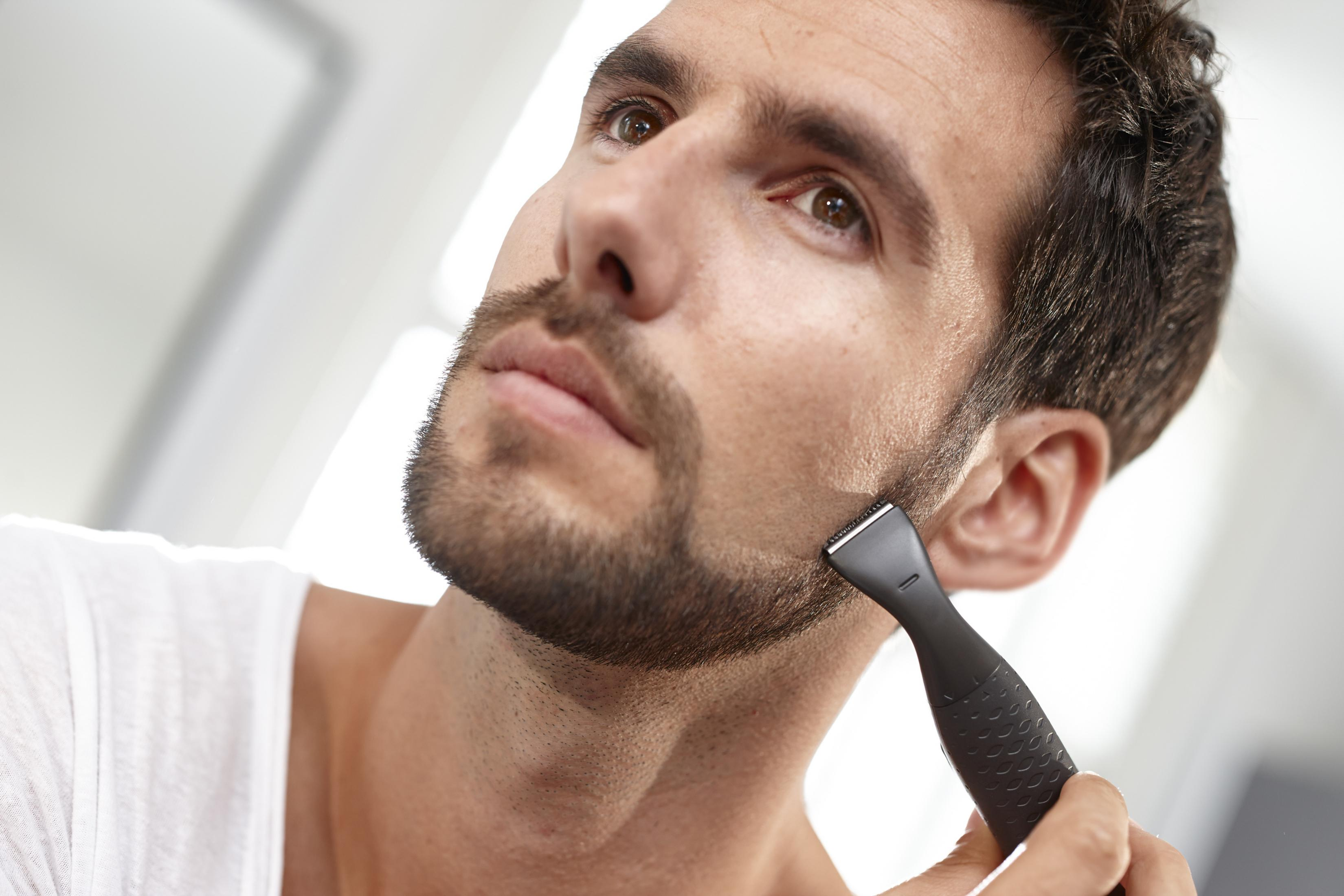 Hombre afeitándose la barba con una recortadora, primer plano, mirando hacia arriba.