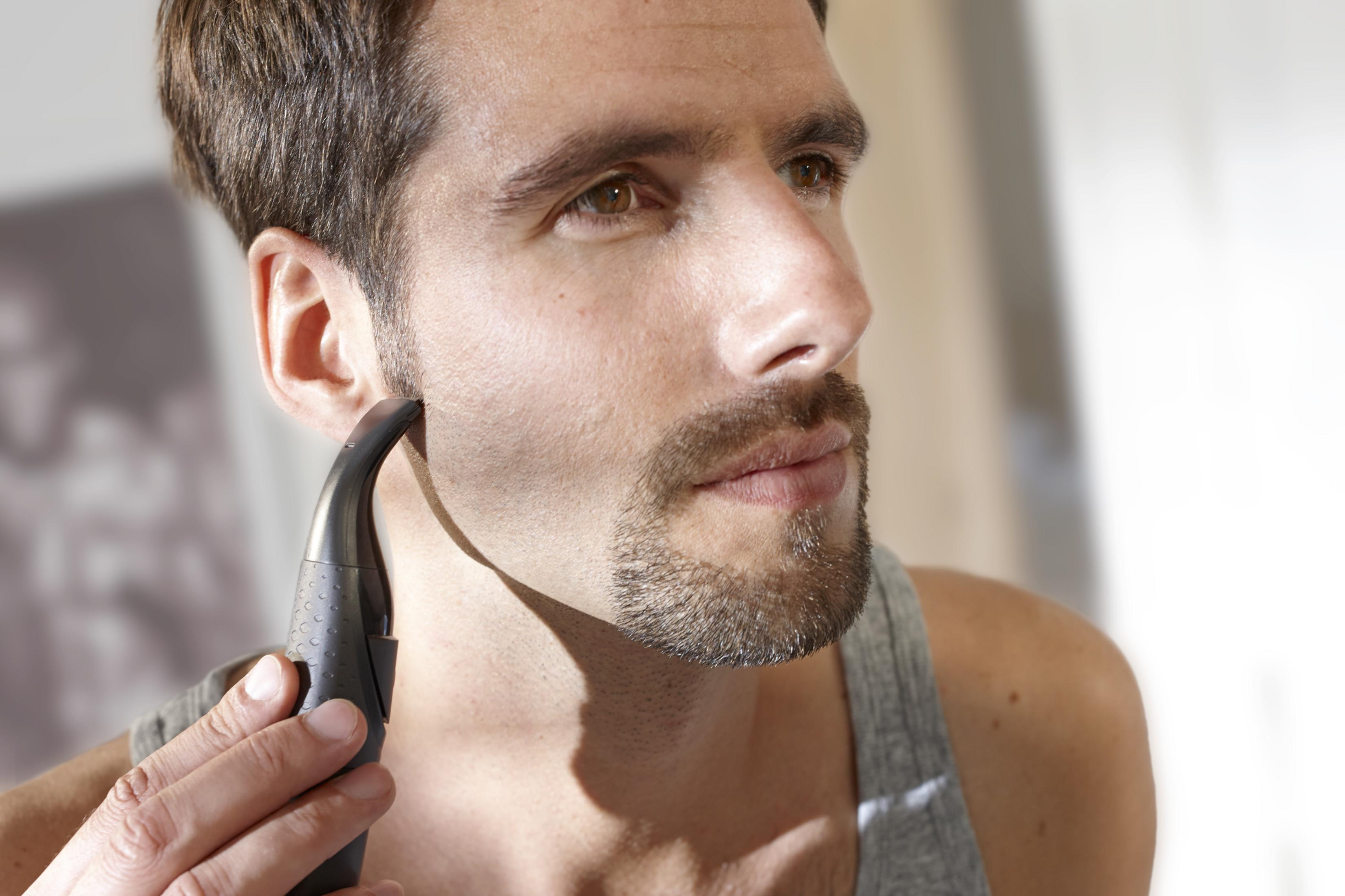 Hombre afeitándose la barba con una recortadora eléctrica negra, primer plano.