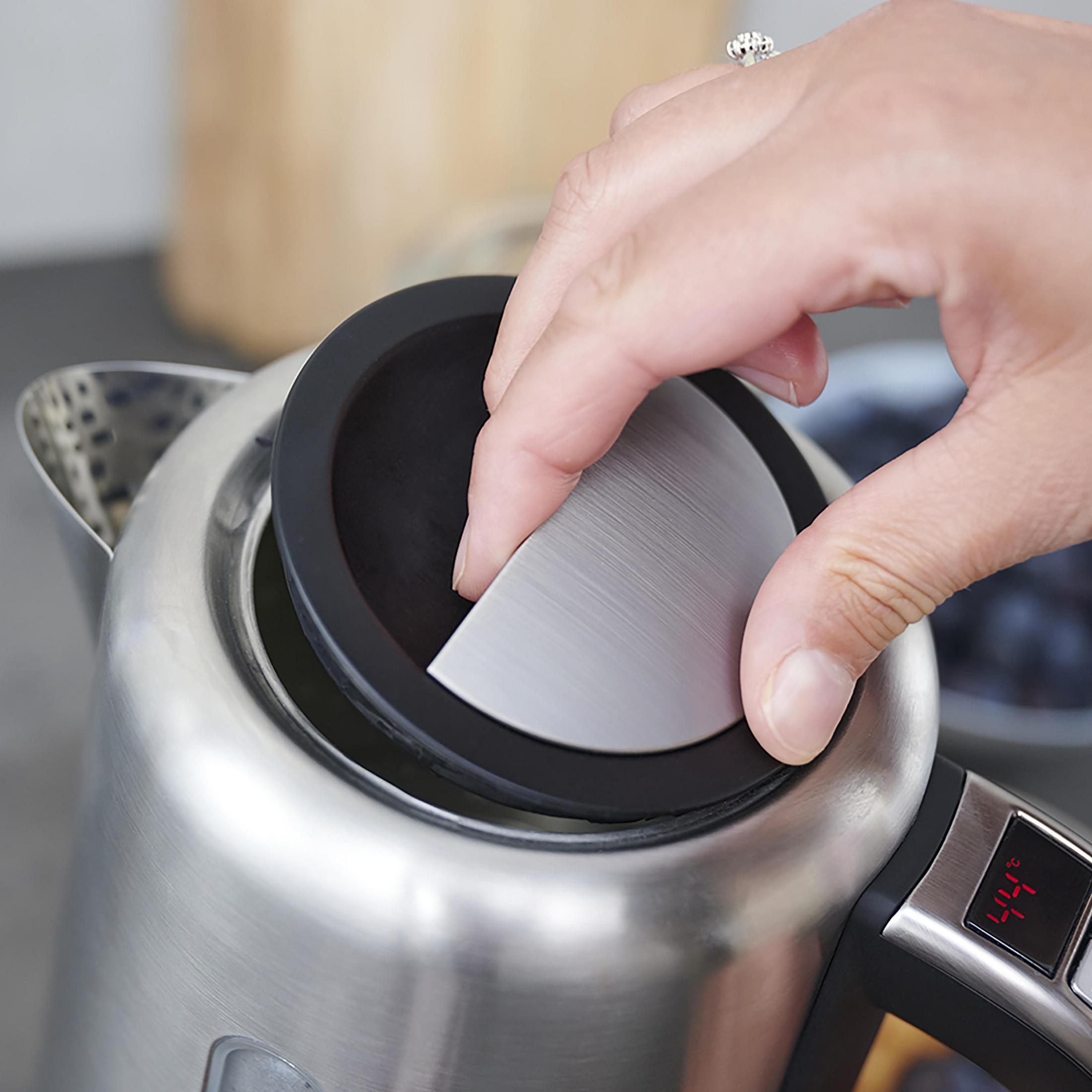 Dłoń otwiera pokrywkę czajnika. Czajnik jest ze stali nierdzewnej.