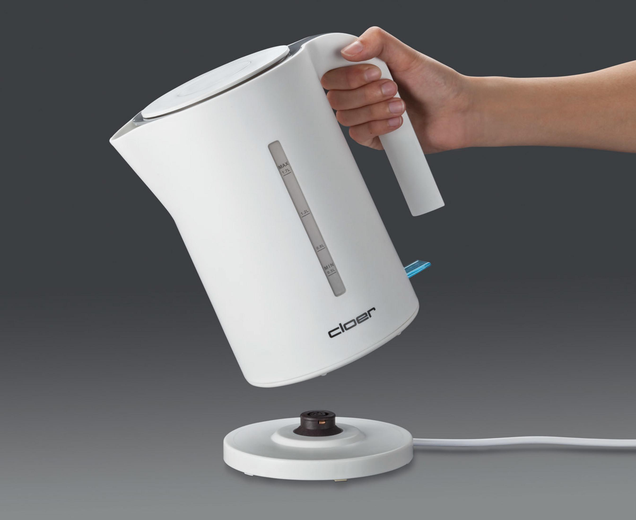 Ein weißer Wasserkocher wird von einer Hand gehalten. Der Wasserkocher steht auf einer Basis, der Hintergrund ist grau.
