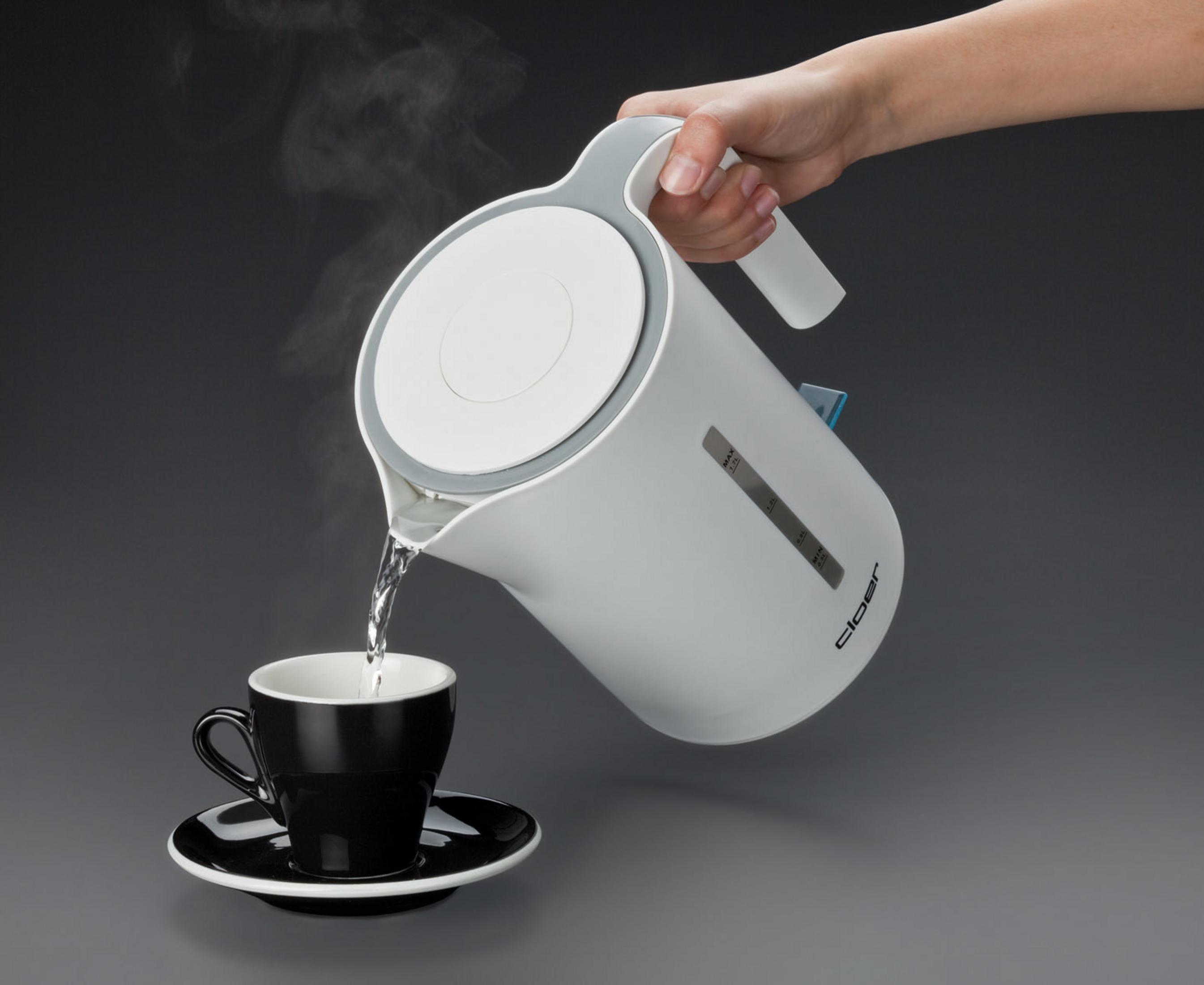Ein weißer Wasserkocher gießt Wasser in eine schwarze Tasse auf einer schwarzen Untertasse. Grauer Hintergrund.