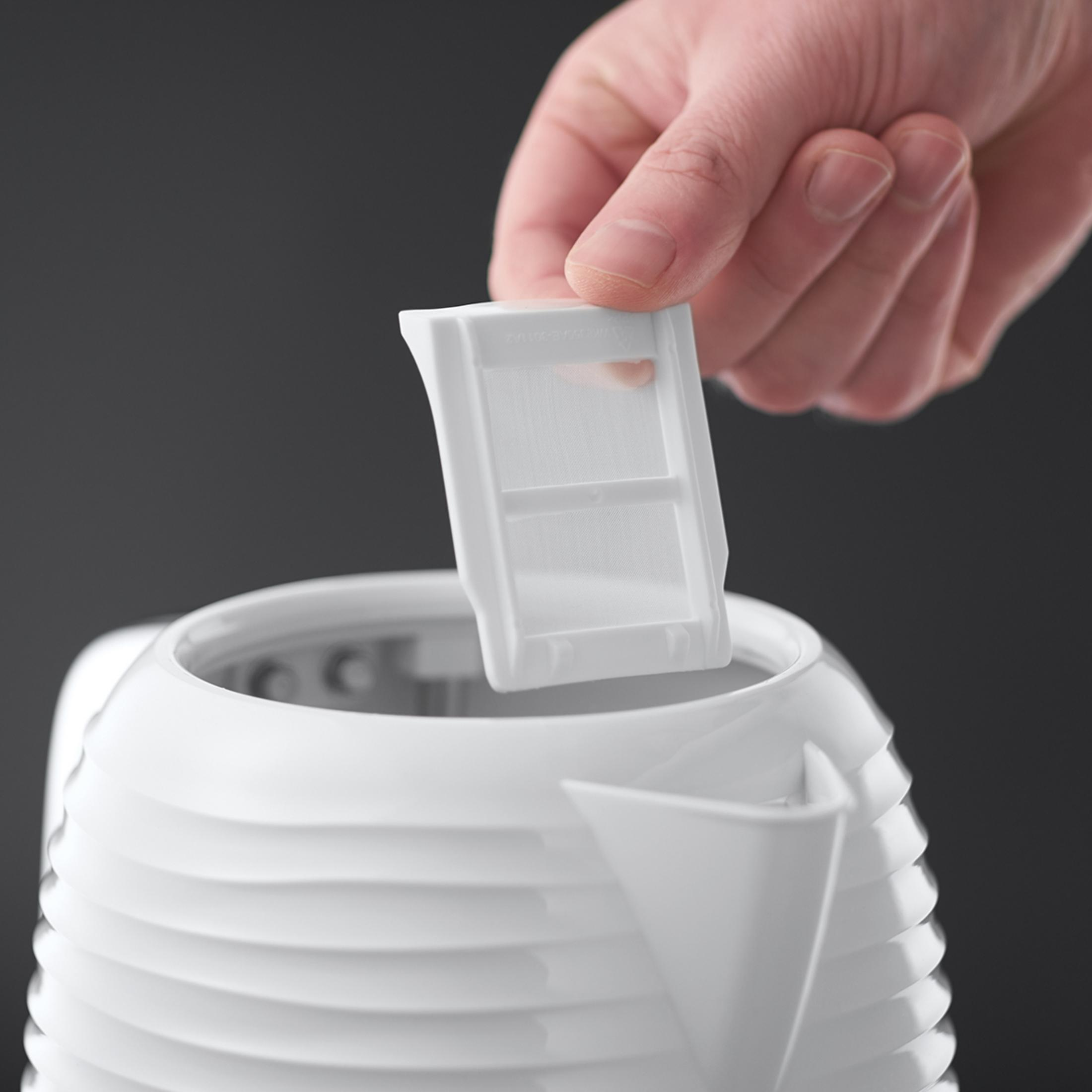 Ręka wkładająca biały filtr do białego czajnika o żebrowanym wzorze, na czarnym tle.