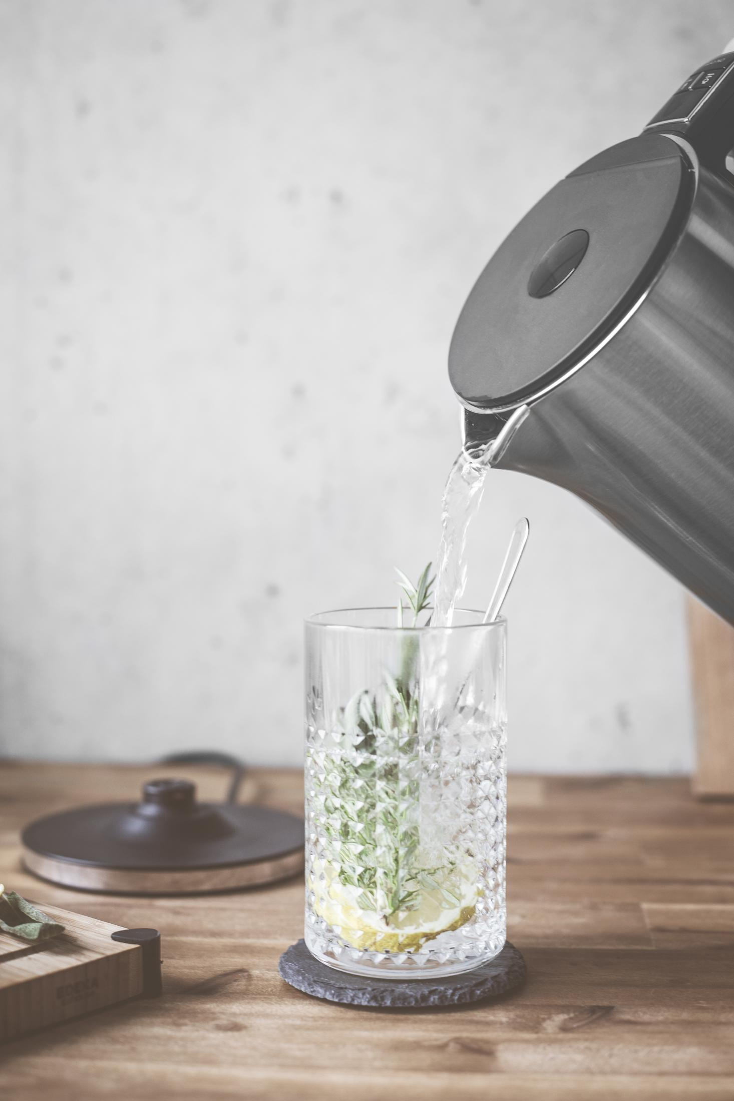 Czajnik nalewający wodę do szklanki z cytryną, rozmarynem i łyżeczką.