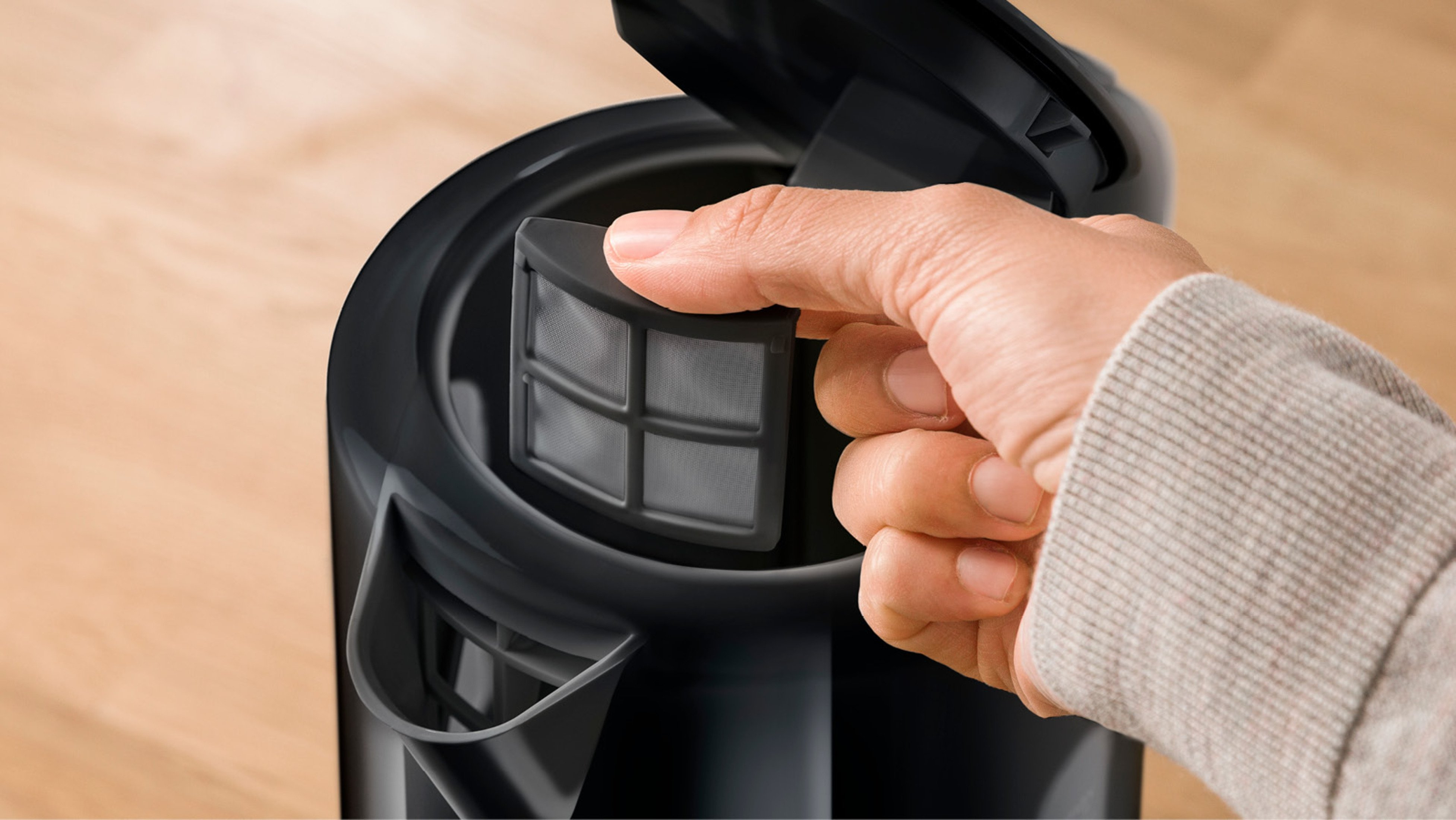 Primo piano di una mano che rimuove un filtro da un bollitore elettrico nero.