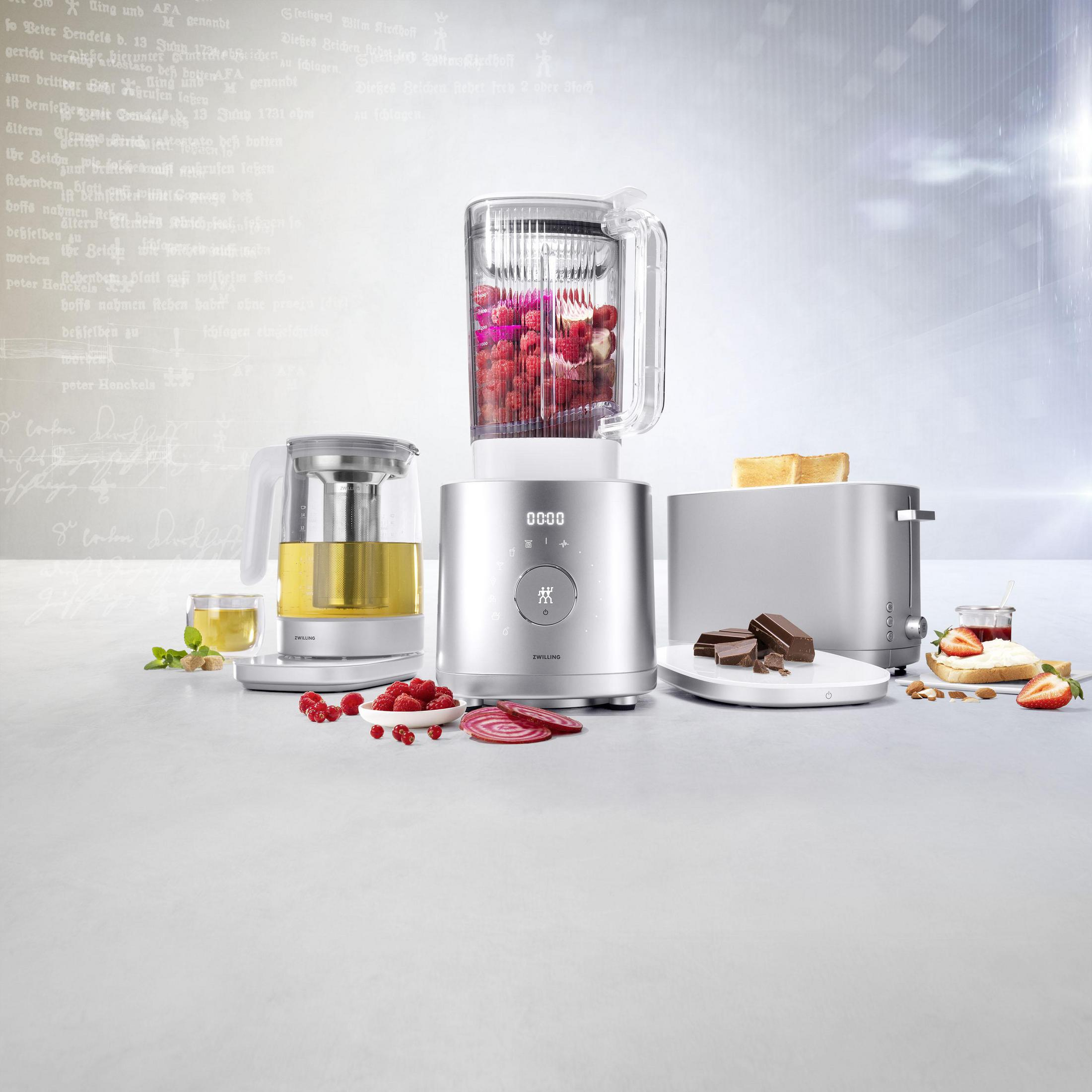 Sprzęt kuchenny na stole: blender z owocami, czajnik do herbaty, toster, z jedzeniem.